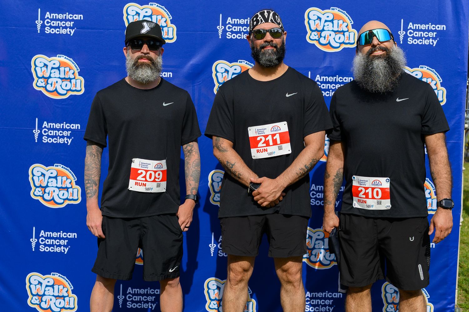 Three bearded men in black Nike shirts wear race bibs at an American Cancer Society Walk & Roll event.