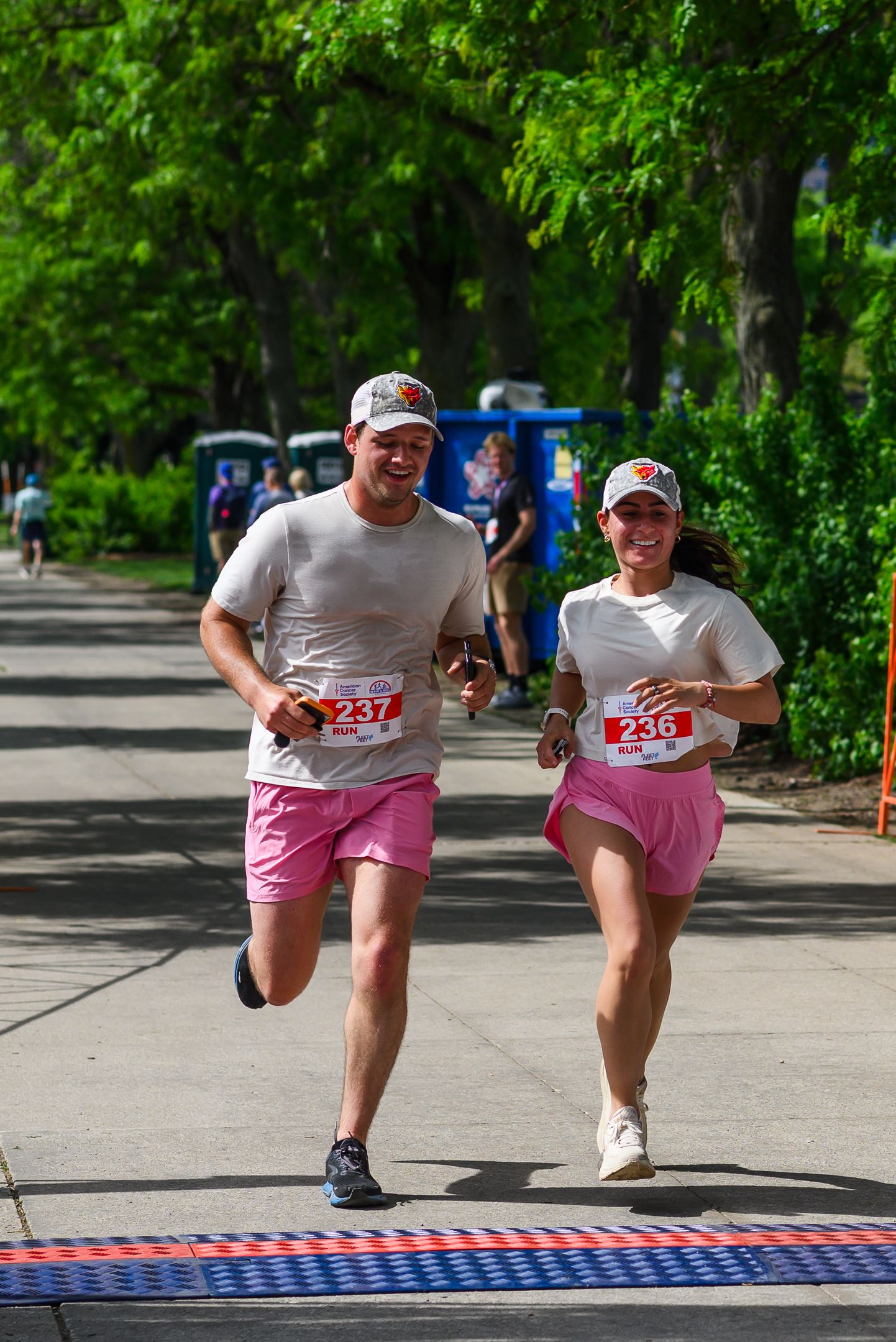 Two runners in matching pink shorts cross finish line at Walk & Roll charity race.