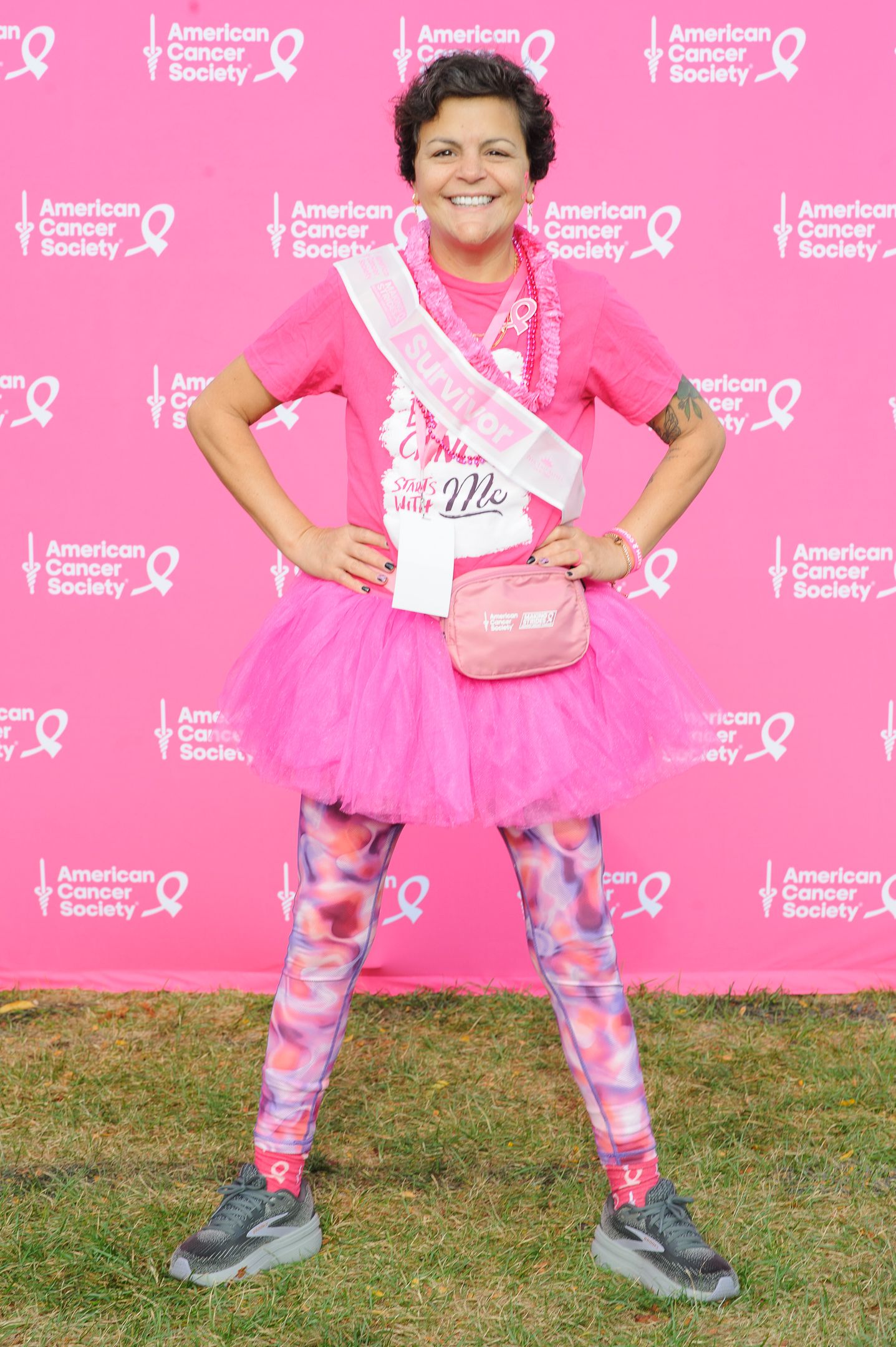 Supporter wearing pink tutu and tie-dye leggings poses energetically at cancer awareness event.