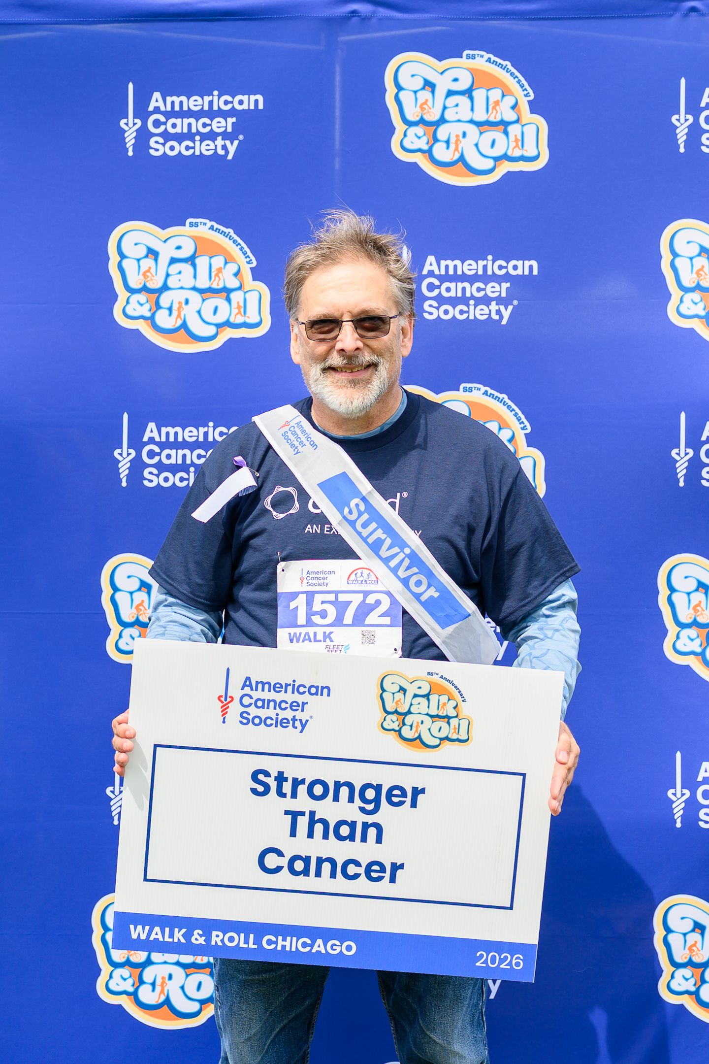 Cancer survivor holds Stronger Than Cancer sign wearing sash at Walk & Roll Chicago ACS event.