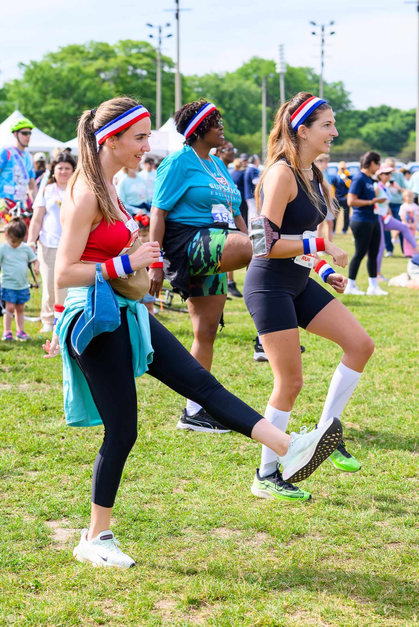 Three women in athletic wear with red white and blue headbands jog together at outdoor charity run event.