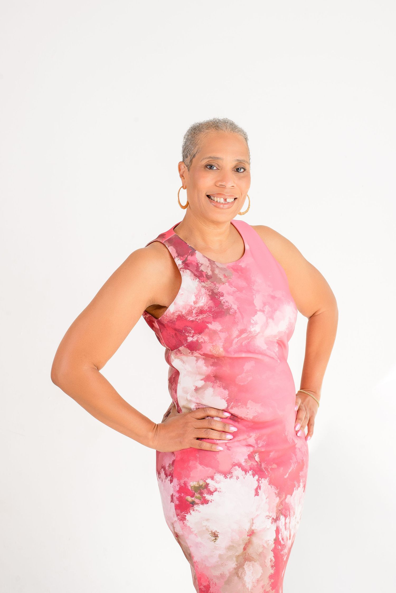 A person wearing a pink and white tie-dye dress poses confidently in a studio setting against a white background.