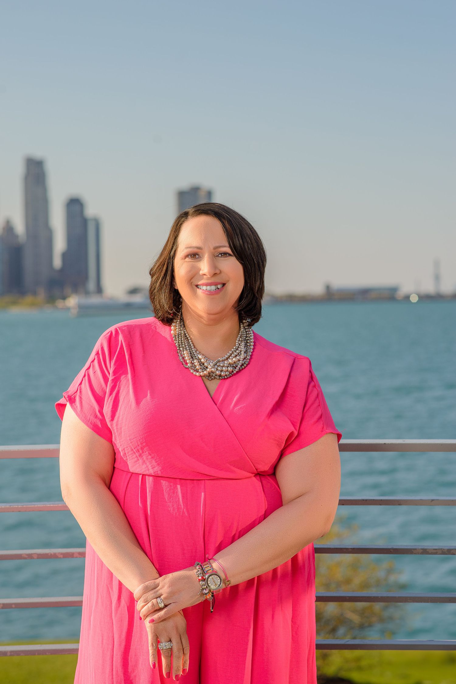 Person in bright pink wrap dress poses on waterfront deck with Chicago skyline visible in background.