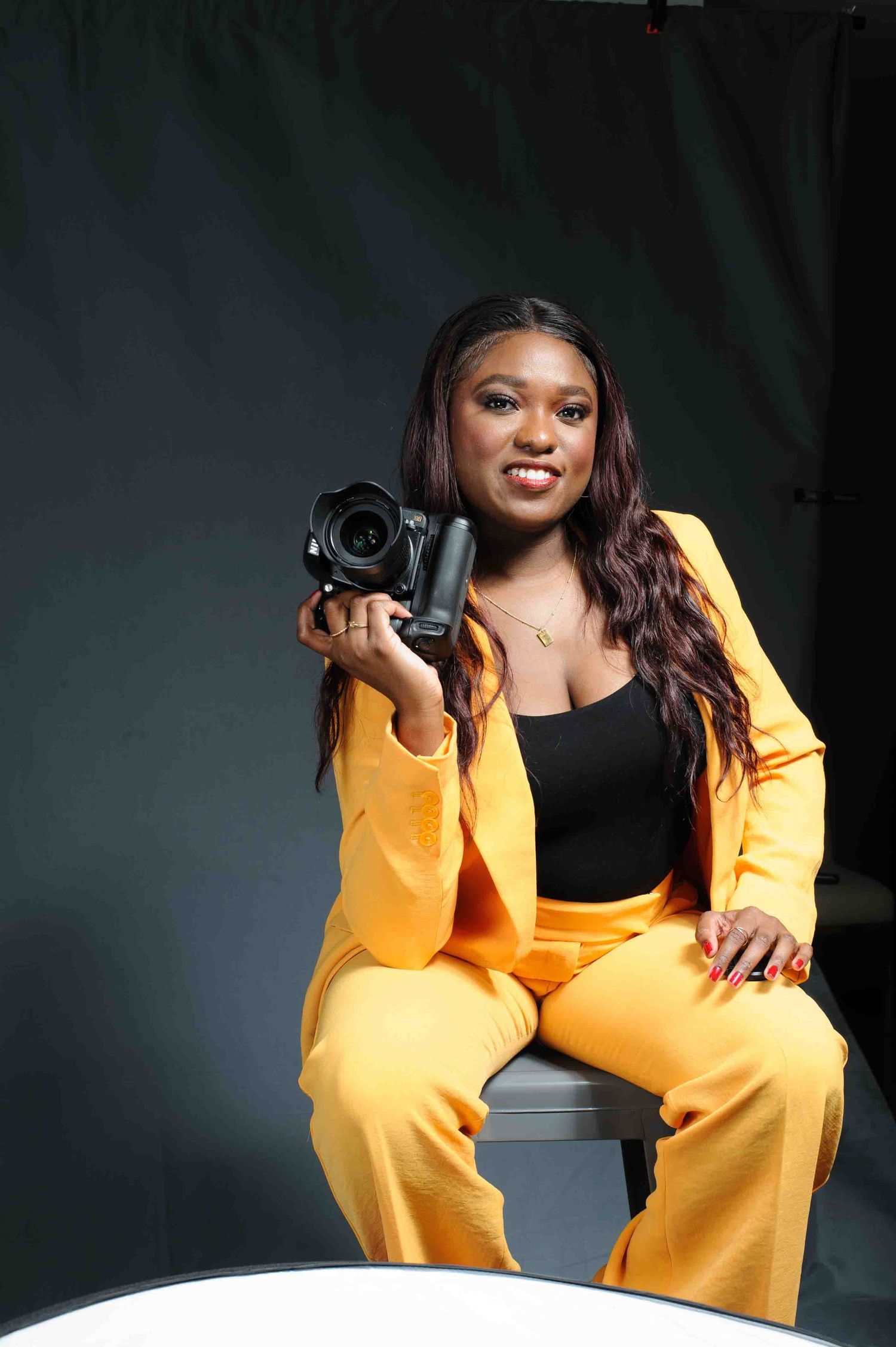 Professional photographer in vibrant yellow suit sits with camera while posing during studio photoshoot.