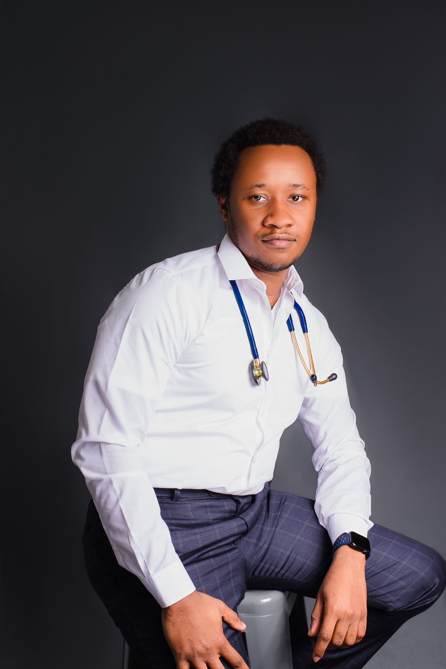 Professional studio portrait of someone in a white dress shirt and navy pants kneeling against dark background.