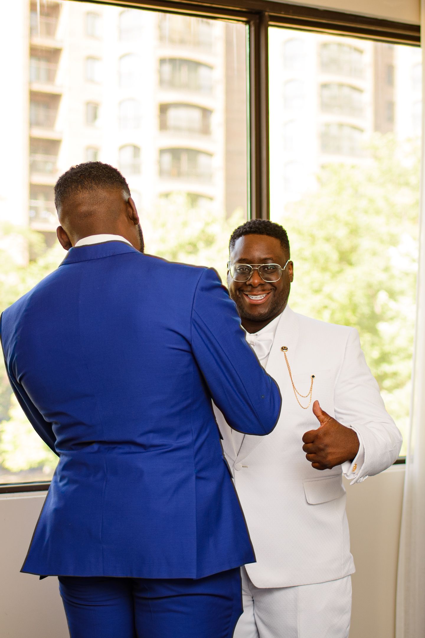 Two people in business attire share a friendly embrace in an office setting with bright natural lighting.
