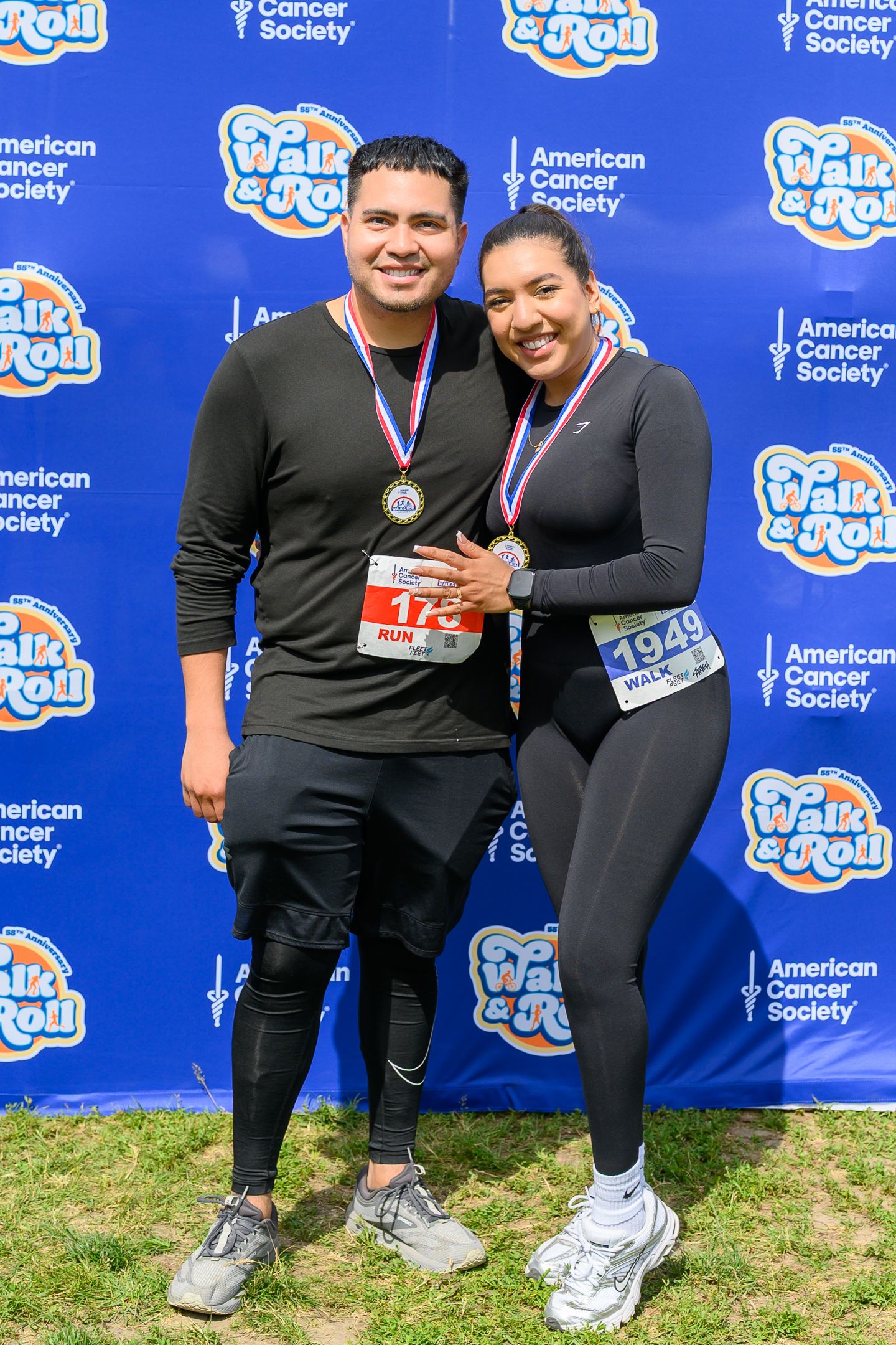 Two participants wearing medals pose at American Cancer Society Walk & Roll event in matching black athletic wear.