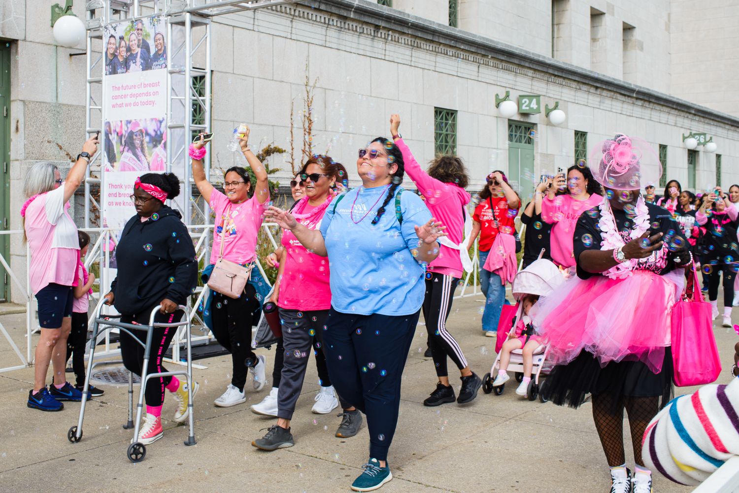 Participants in pink attire walking together during a charity event or awareness walk along a city street.
