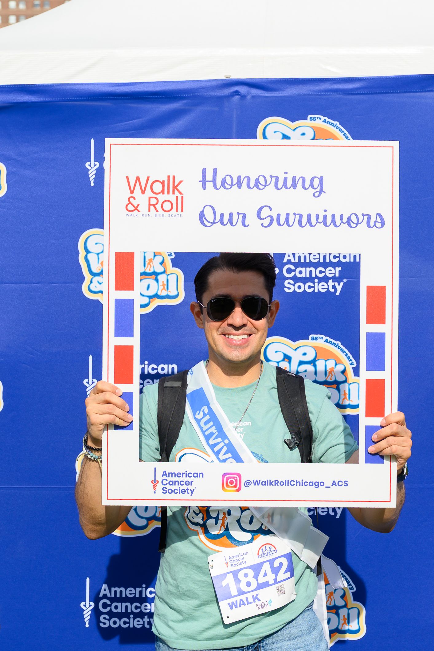 A smiling cancer survivor holds an American Cancer Society Walk & Roll 'Honoring Our Survivors' photo frame at a charity event.