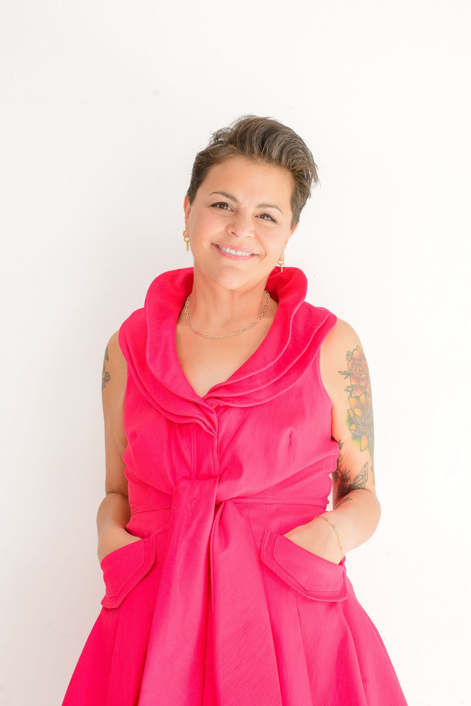 Person wearing a bright pink sleeveless dress with bow detail poses against white background.