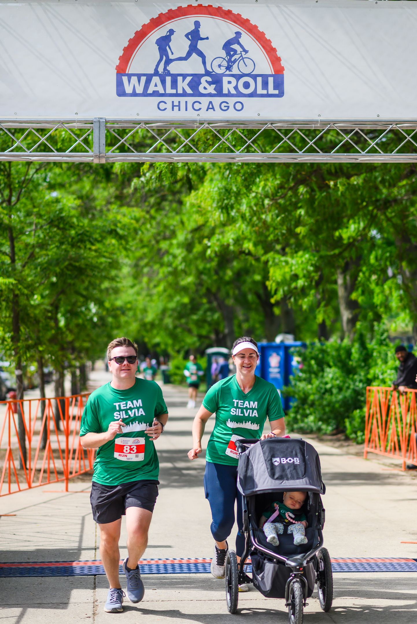 Team Silvia runners in green shirts cross Walk & Roll Chicago finish line with a jogging stroller.