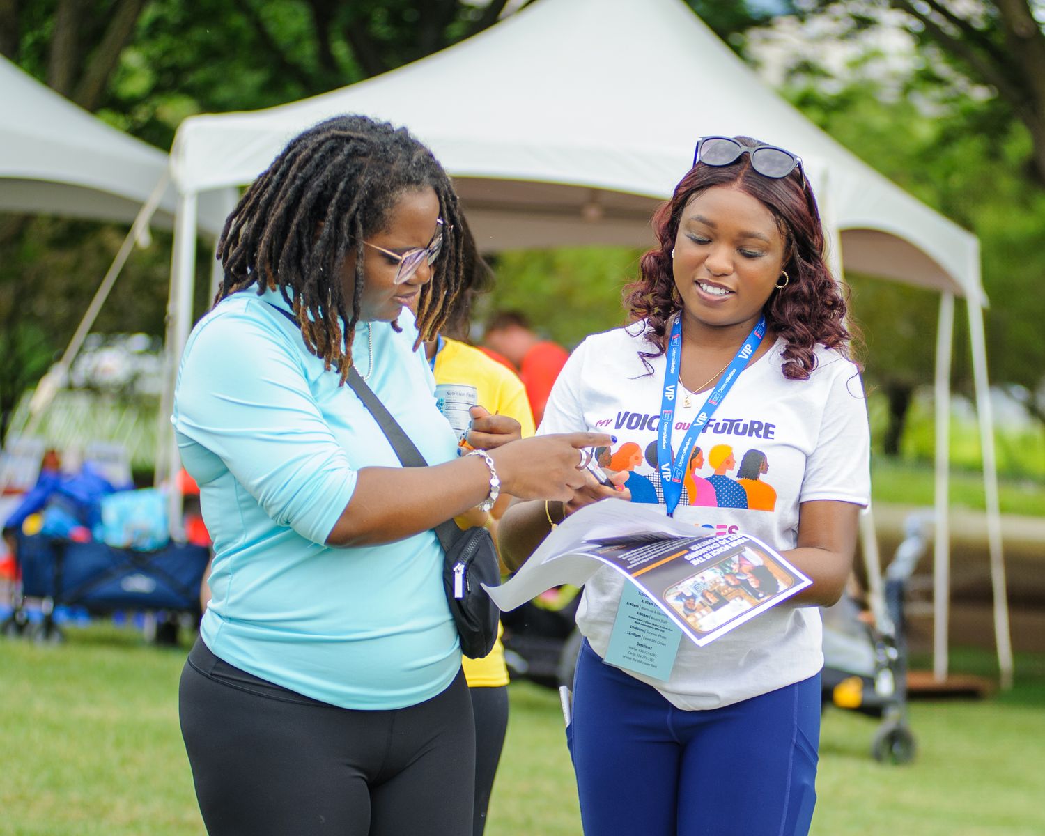 Two people in light blue and white shirts enjoying an outdoor event with tents in the background.