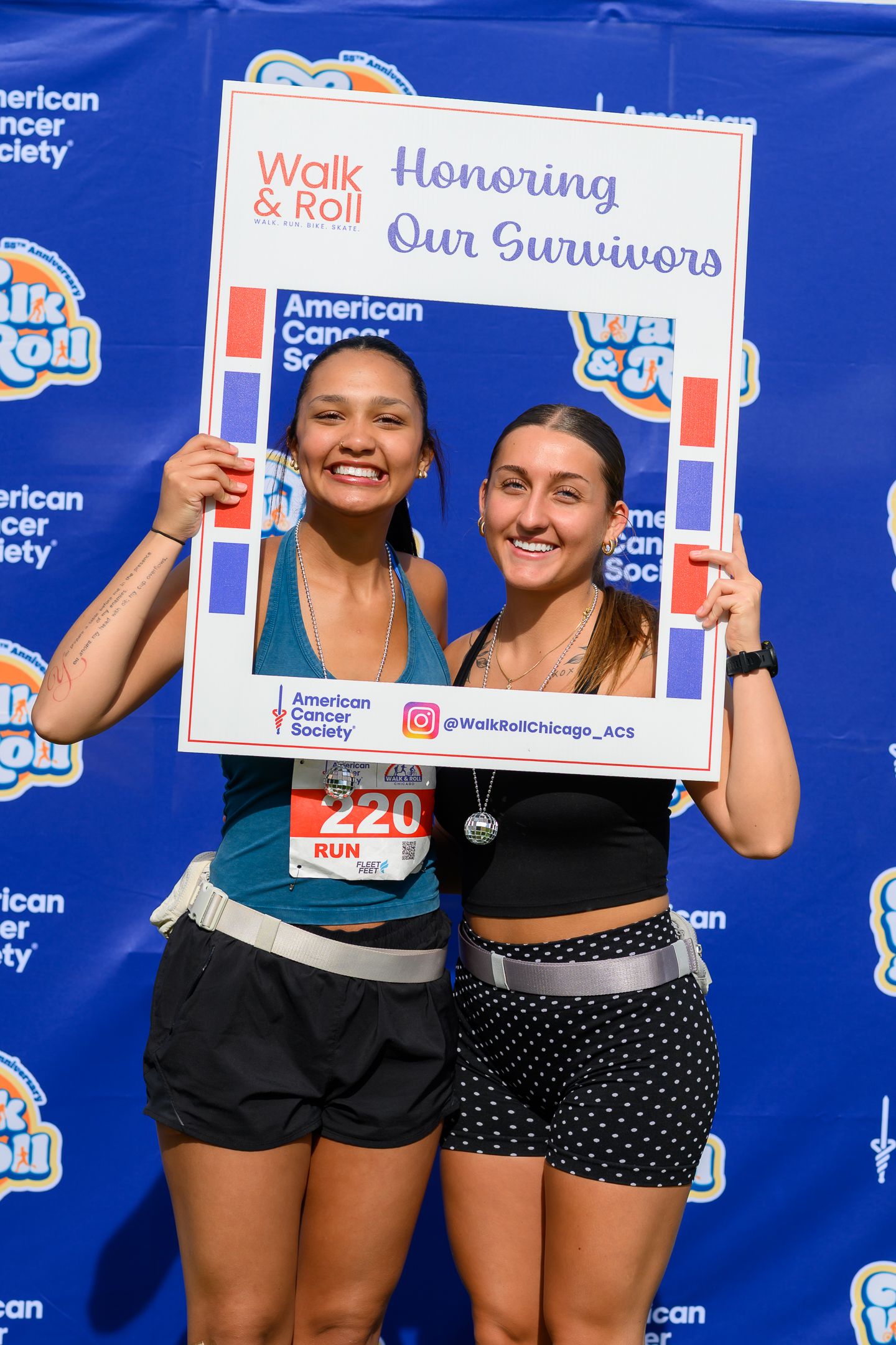 Two women smile holding Honoring Our Survivors photo frame at Walk & Roll Chicago charity run event.
