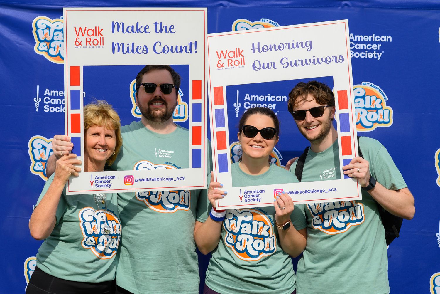 Four people holding Walk & Roll American Cancer Society fundraiser signs, smiling outdoors at a charity event.