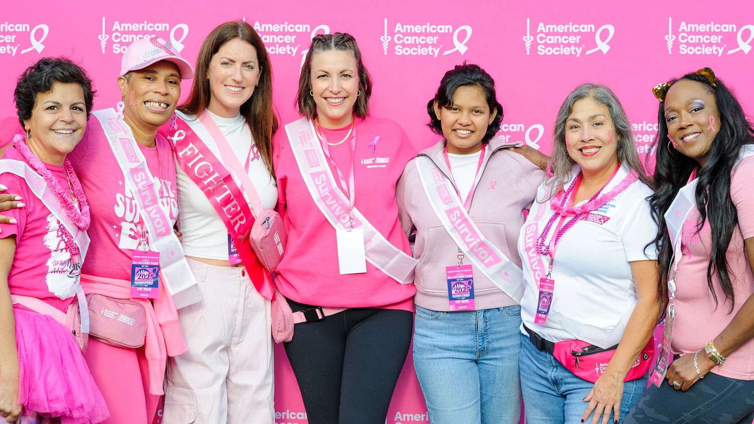 Group photo of participants wearing pink and white at American Cancer Society event against pink backdrop.