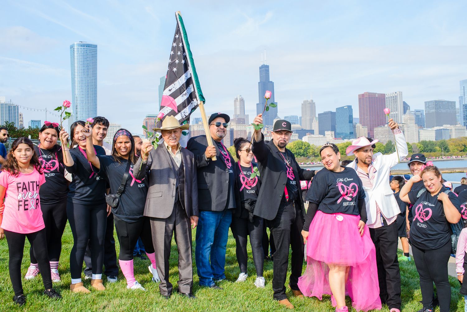 A large group of people in pink and black attire gather outdoors for a charity event with city skyline in background.