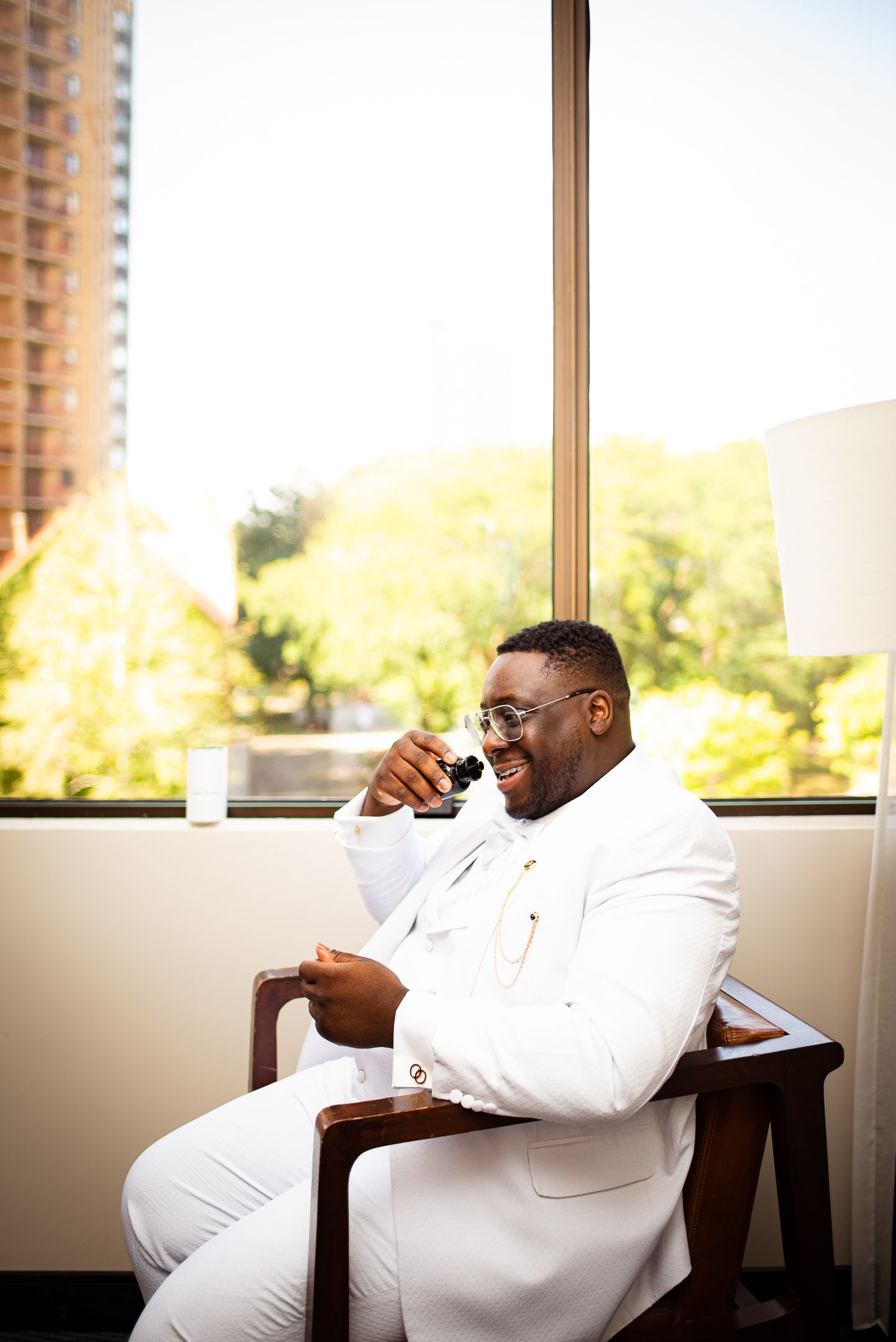 Man relaxing in white suit by window with city view.