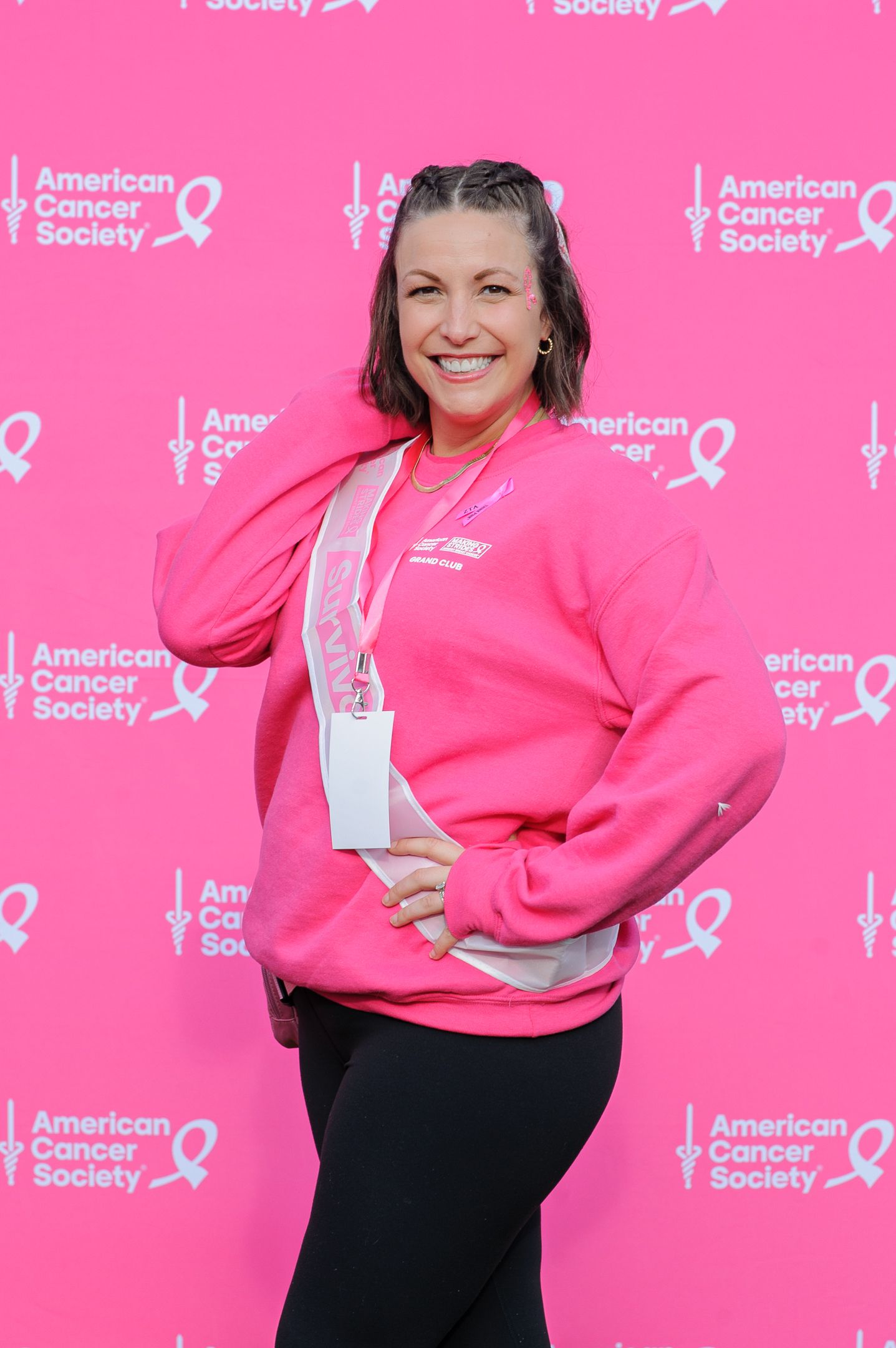 Woman in bright pink sweatshirt poses against pink backdrop with American Cancer Society logos.