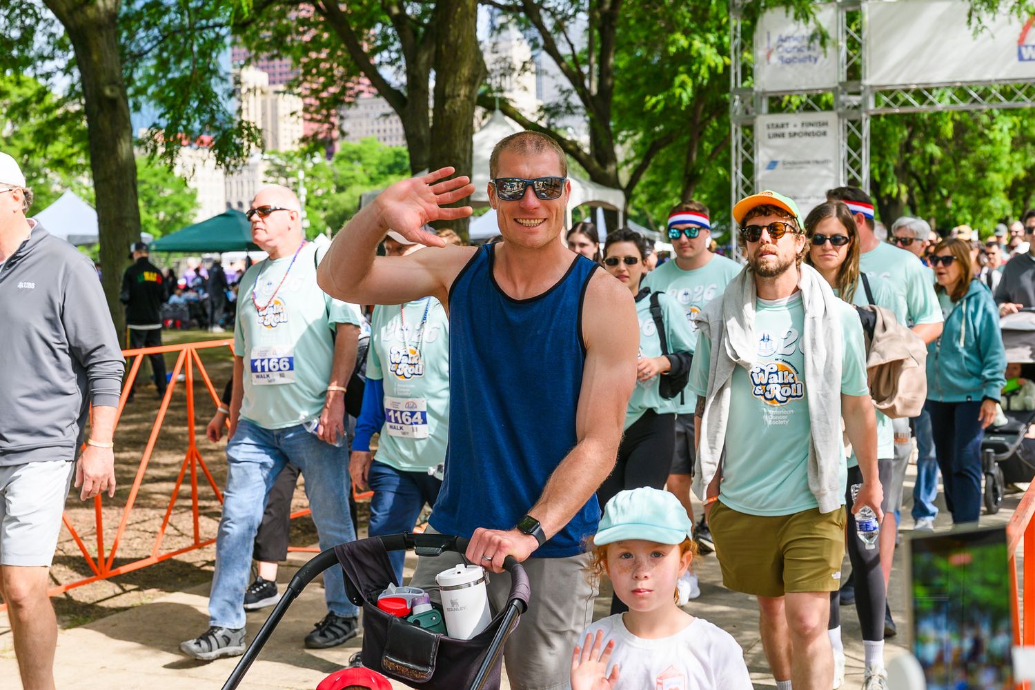 Smiling man pushing stroller waves at camera during American Cancer Society Walk and Roll charity walk.