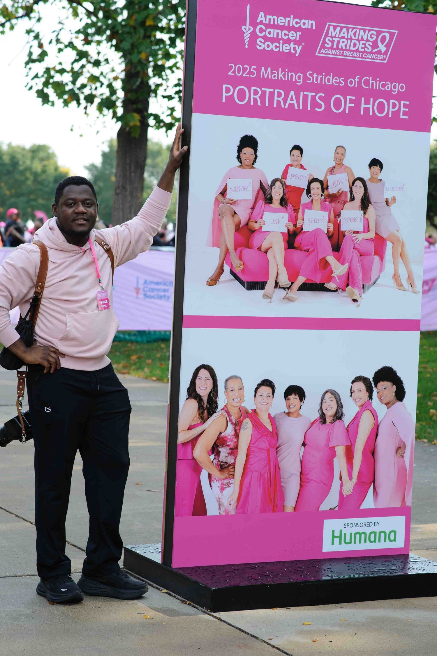Pink and white display boards showing breast cancer awareness campaign portraits and messaging at an outdoor event.