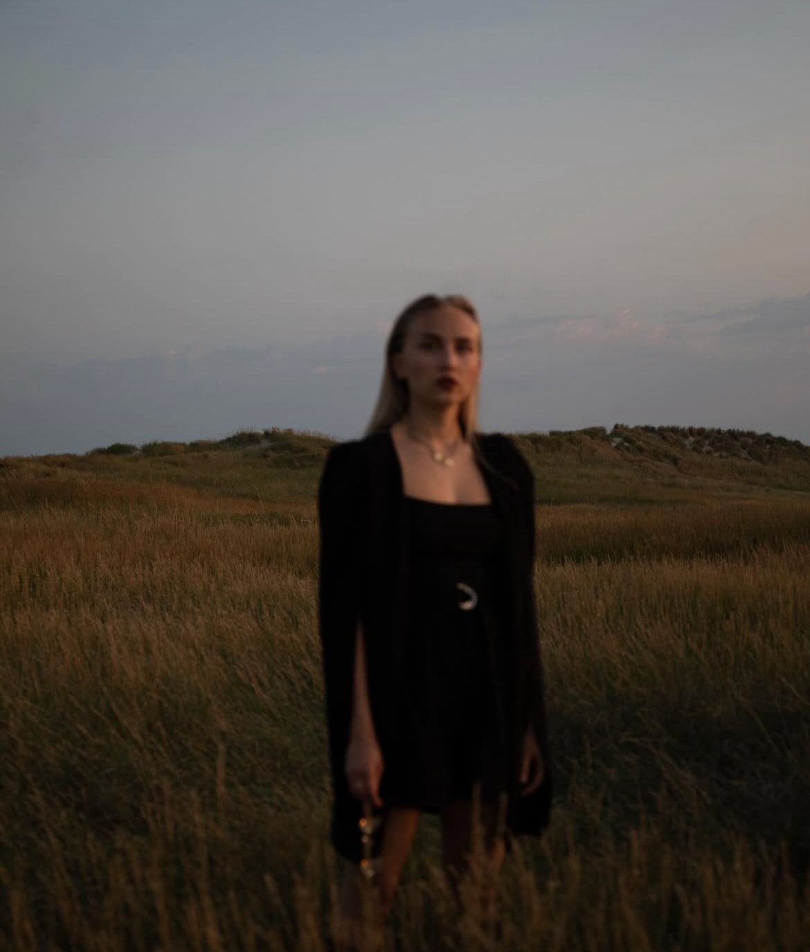 Moody sunset portrait in field wearing black dress against dusky sky.
