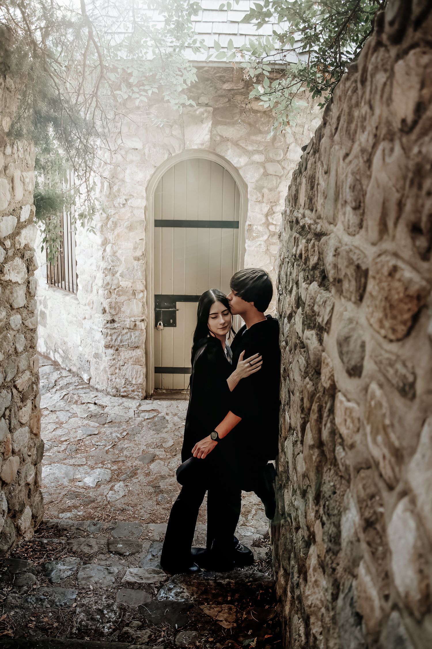 Romantic couple embraces near stone walls and archways in rustic outdoor setting.