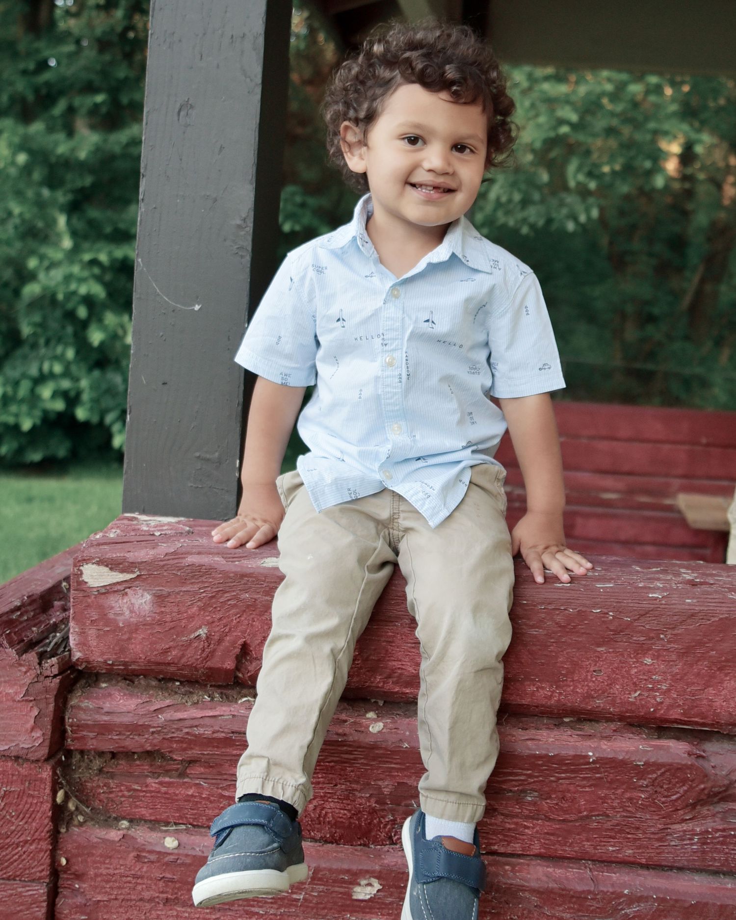 Young child in light blue shirt sitting on red painted wooden steps outdoors.