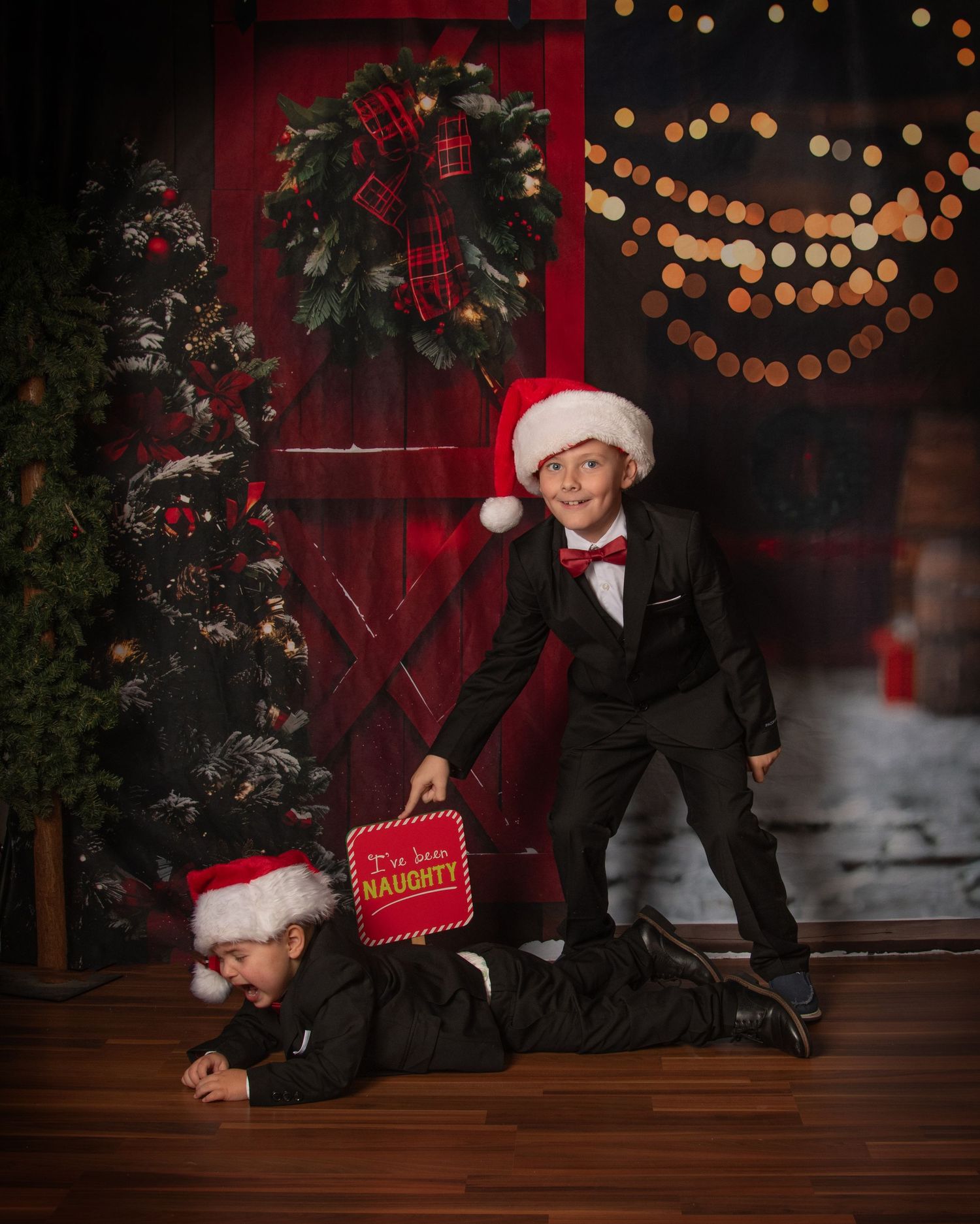 A festive holiday photo session with red backdrop, string lights, and someone wearing a Santa hat holding a red book.
