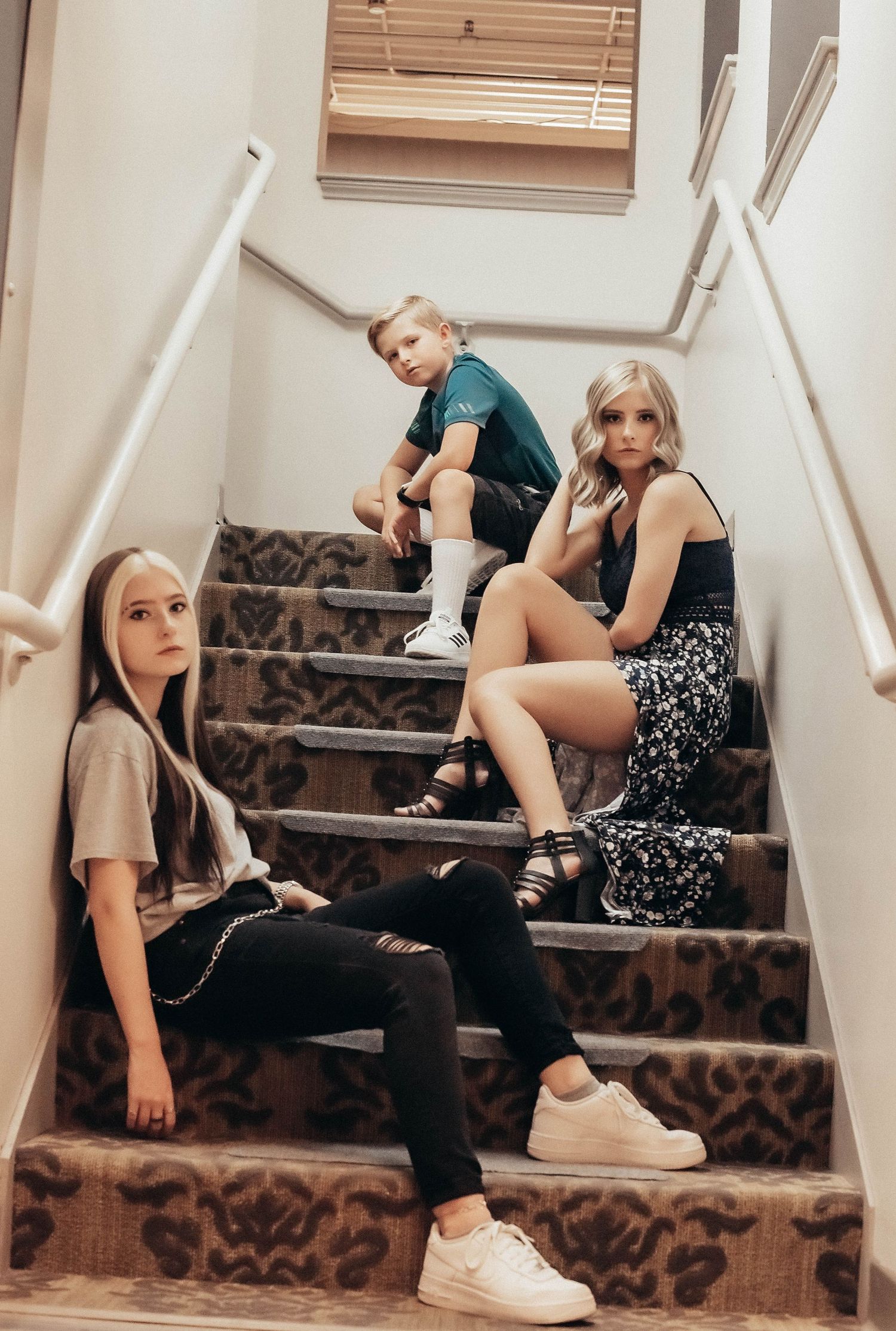 Three friends lounging casually on carpeted stairs in an indoor setting.