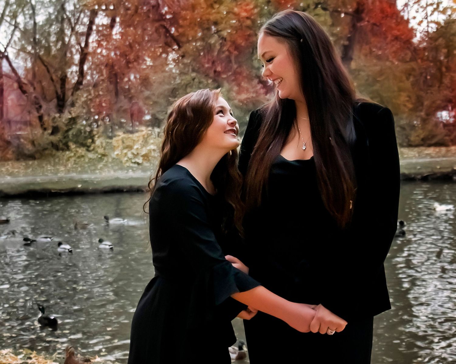 Two people sharing a joyful moment by a pond with fall colors in the background.
