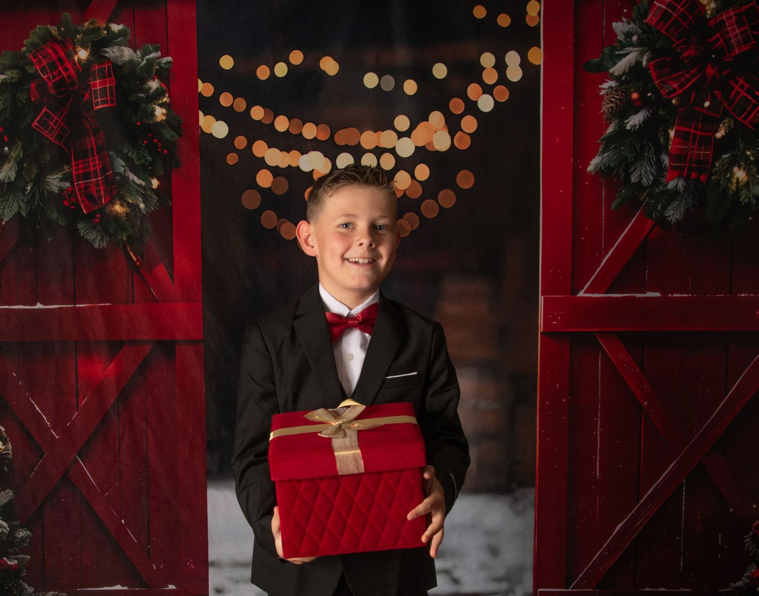 A festive holiday photo session with red velvet decor and warm glowing lights in the background.