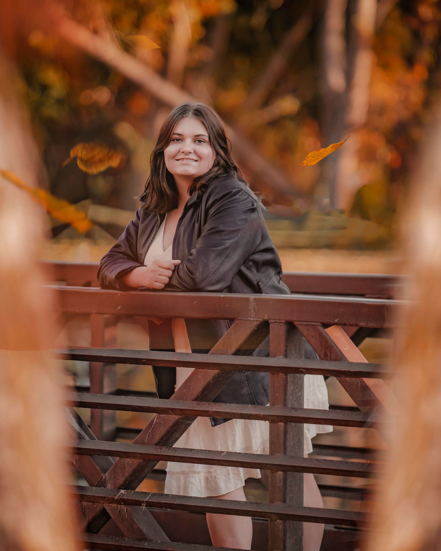 Person in dark jacket leaning on wooden bridge railing surrounded by autumn foliage.