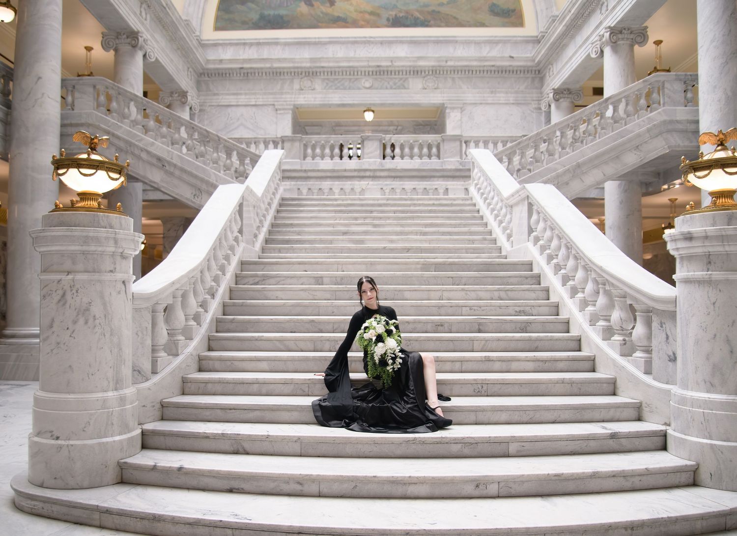 Panoramic view of grand white marble staircase with couple in black attire in elegant government building interior.