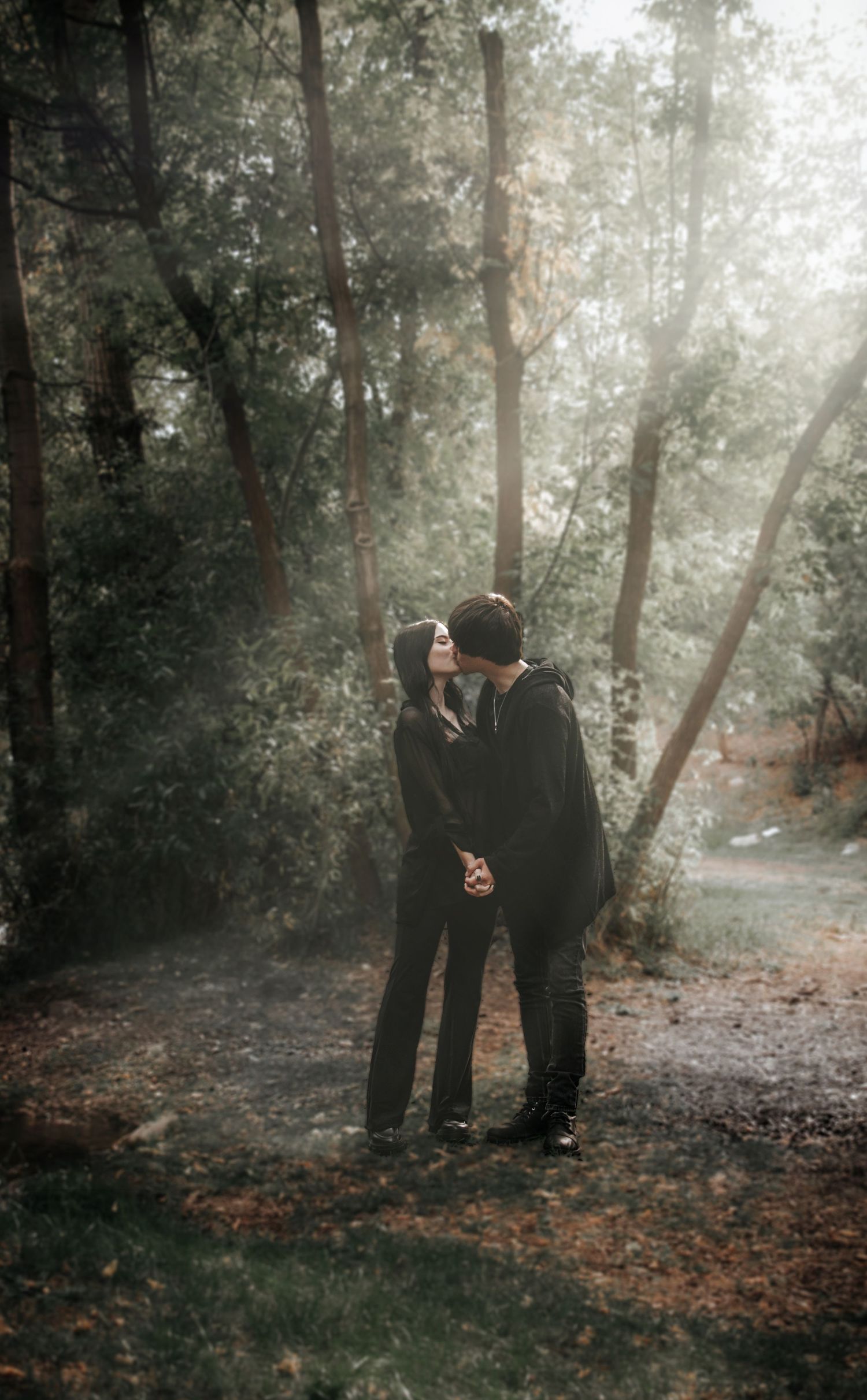 Two figures stand together in a misty autumn forest with sunlight filtering through the trees creating a moody atmosphere.