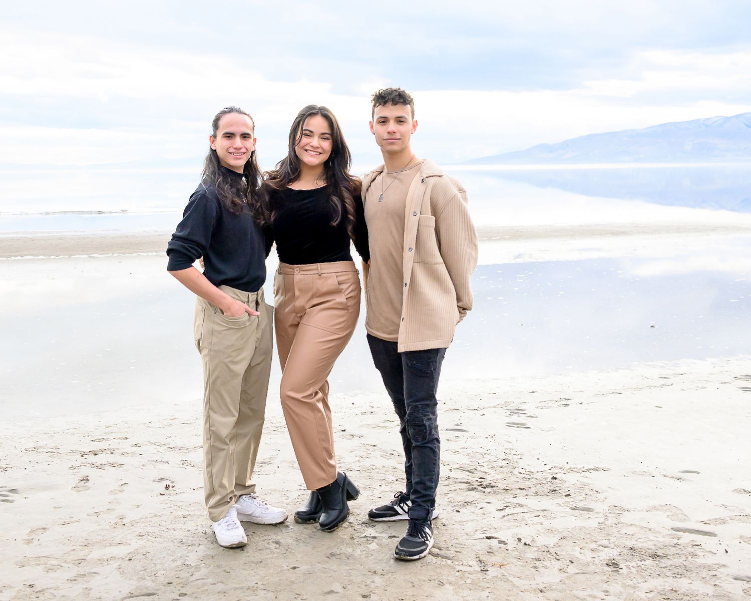 Three people in coordinated neutral tones standing together on a beach.
