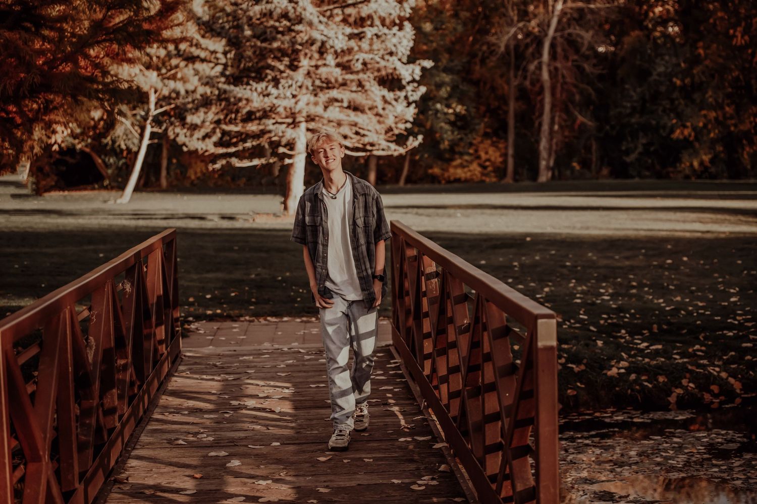 Moody portrait on wooden bridge surrounded by autumn trees and fallen leaves.
