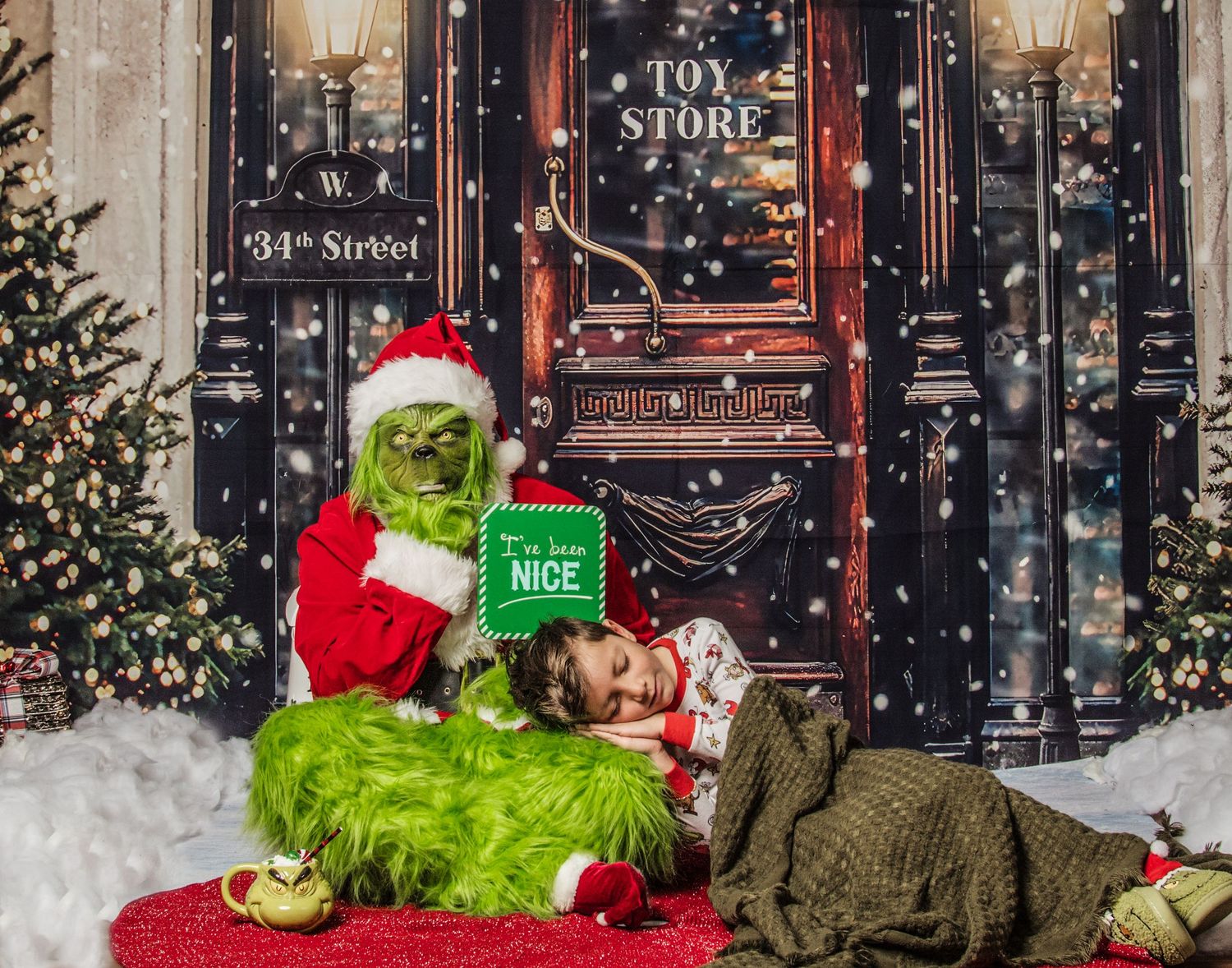 The Grinch in Santa costume sits reading 'How the Grinch Stole Christmas' with a dog beside him in a festive holiday scene.