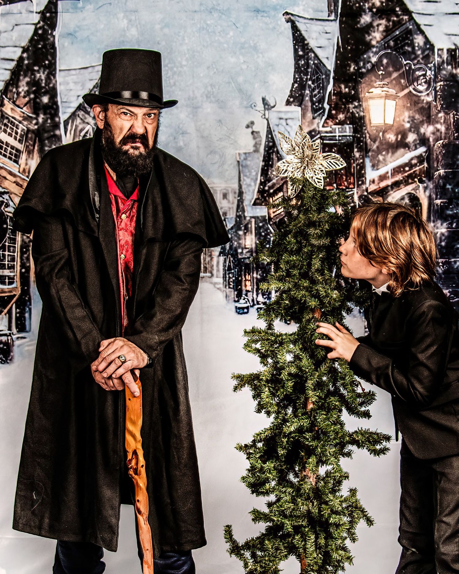 A Victorian-style winter scene with a figure in a long black coat and top hat standing beside a decorated Christmas tree.