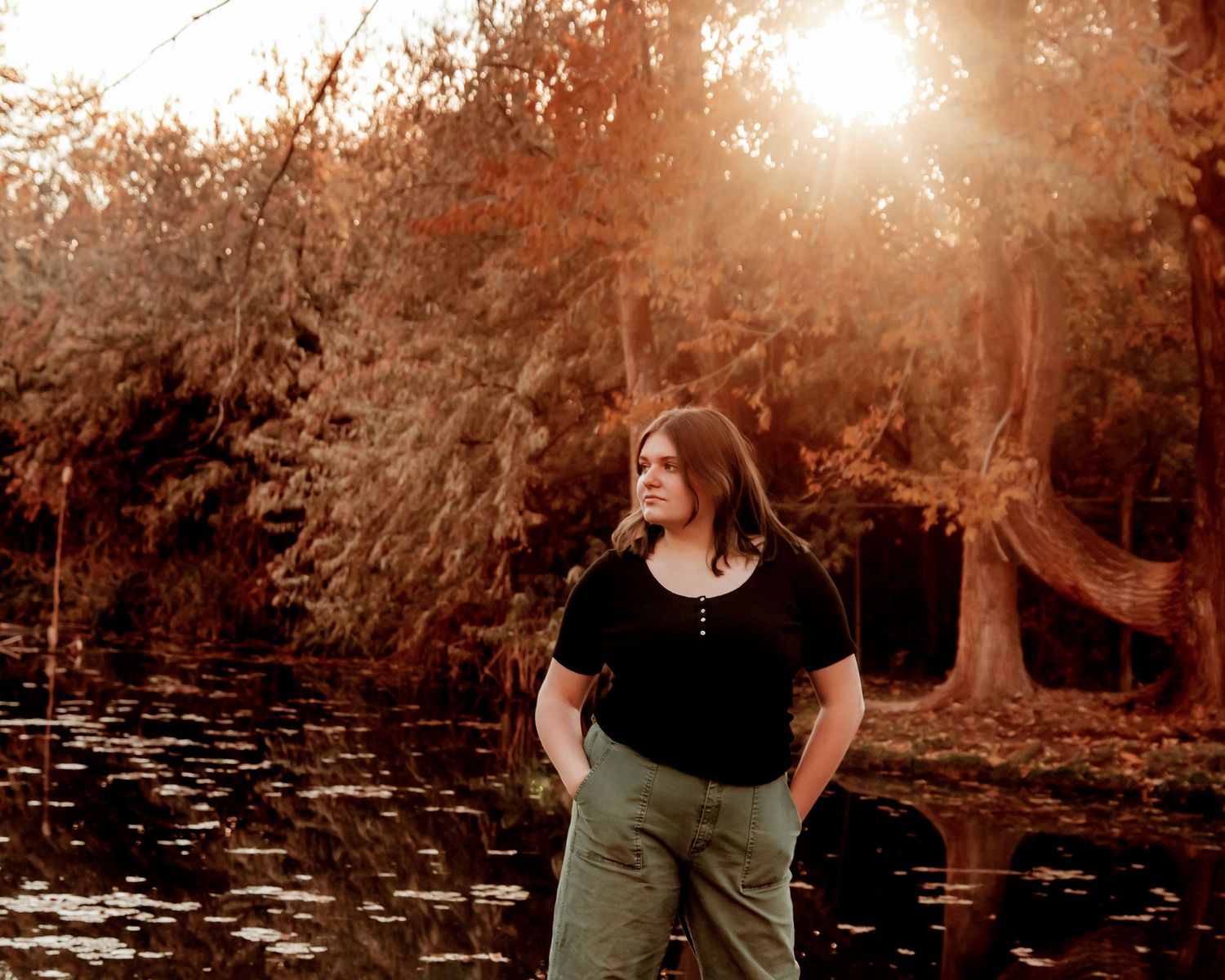 Sunset portrait in nature with person in black shirt against golden autumn trees and pond.