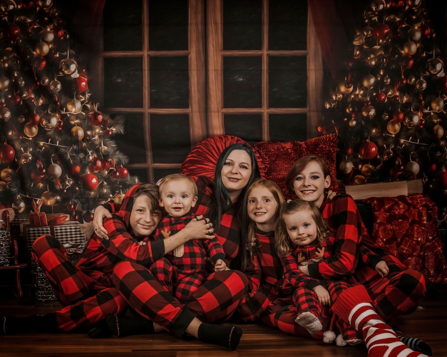 Children in red and black buffalo plaid pajamas pose in front of a decorated Christmas tree for holiday photos.