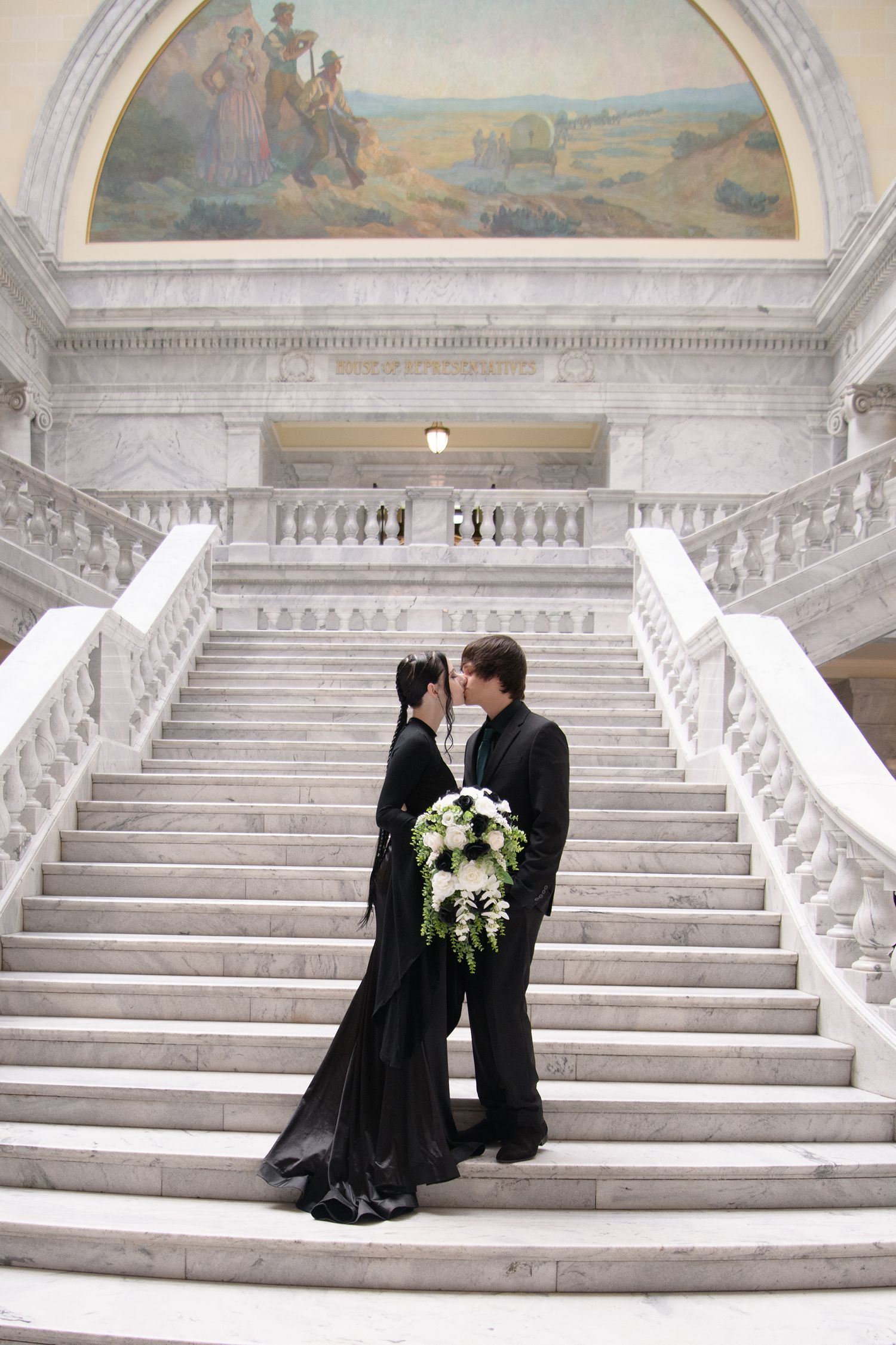 Elegant wedding couple seated on grand marble staircase in formal black attire sharing intimate moment together.