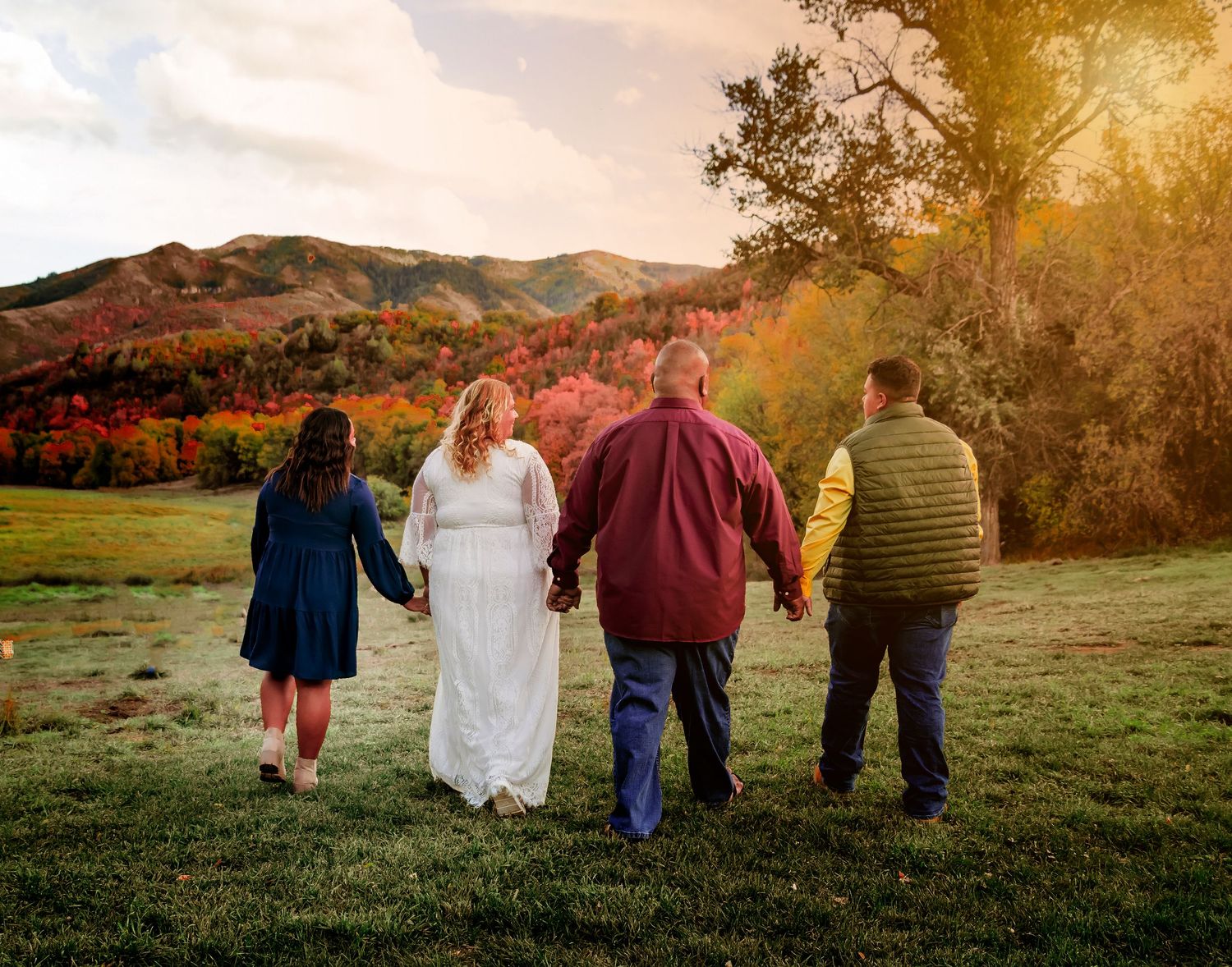 Group walking hand in hand through mountain meadow at sunset with fall foliage.