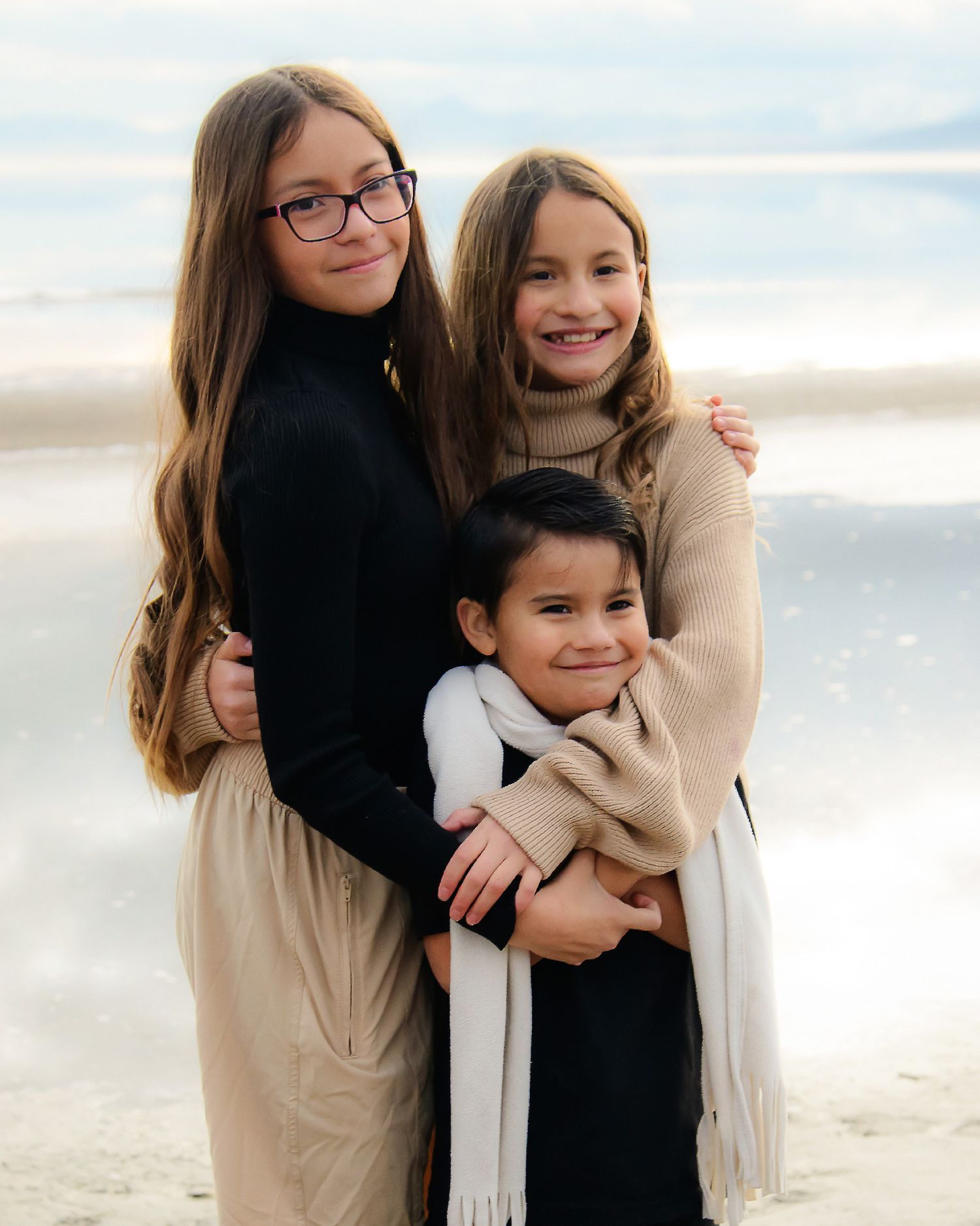 Three young people in warm winter clothing posing together at the beach.