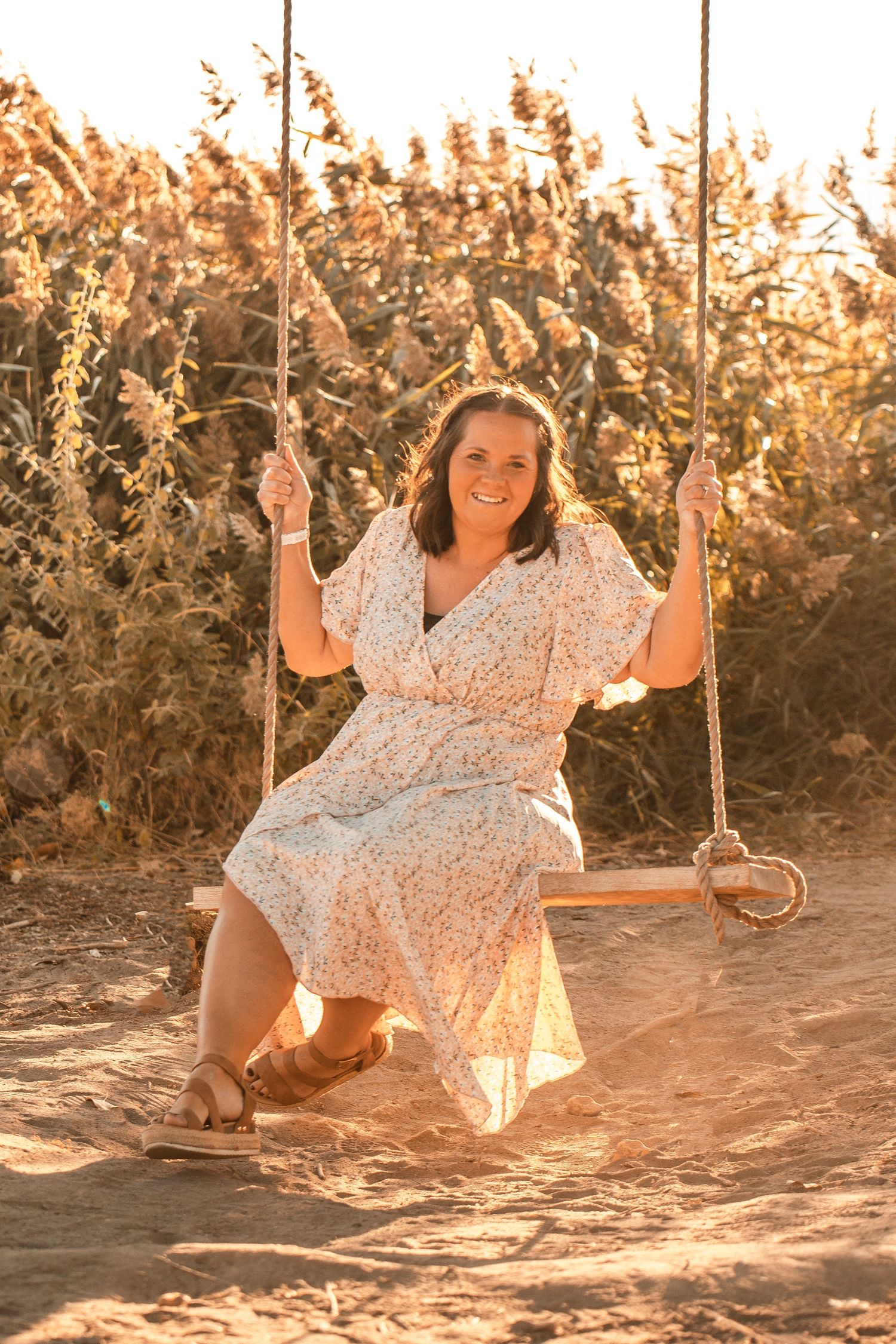 Person on wooden swing in white dress during golden hour surrounded by tall grass and sunlight.