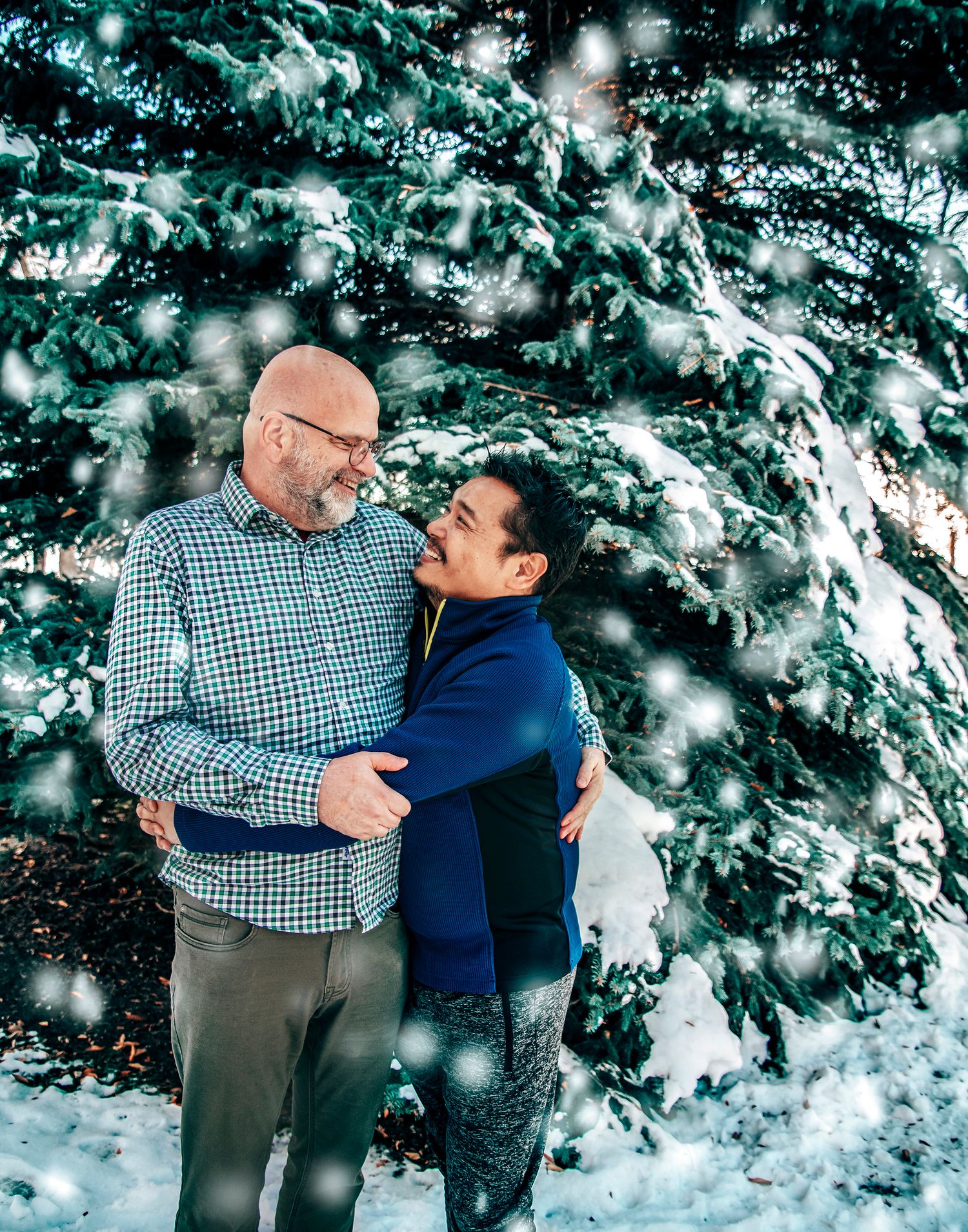 A tender embrace between two people against a snowy evergreen backdrop with falling snowflakes.