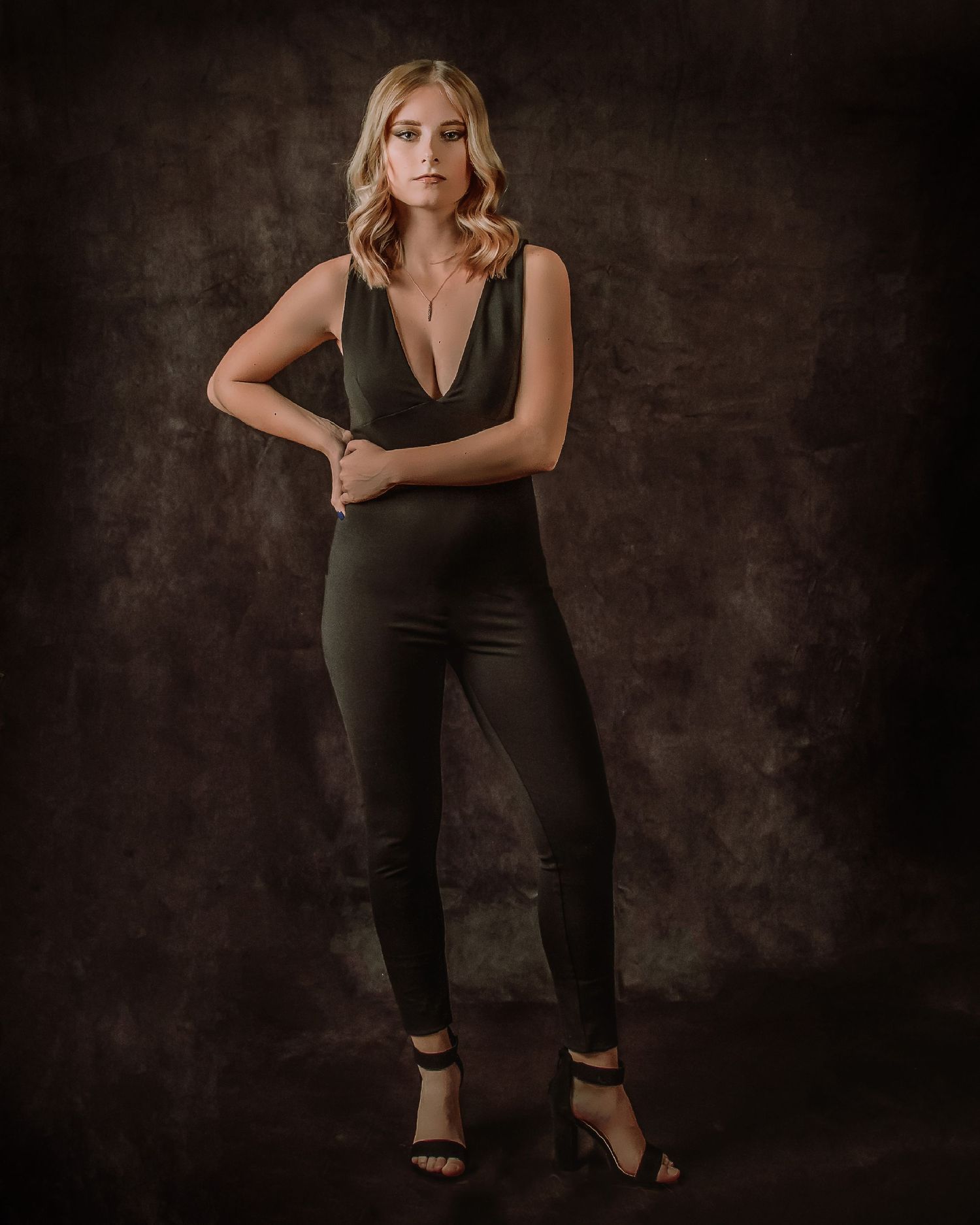 Elegant fashion portrait in black outfit against dark moody background.