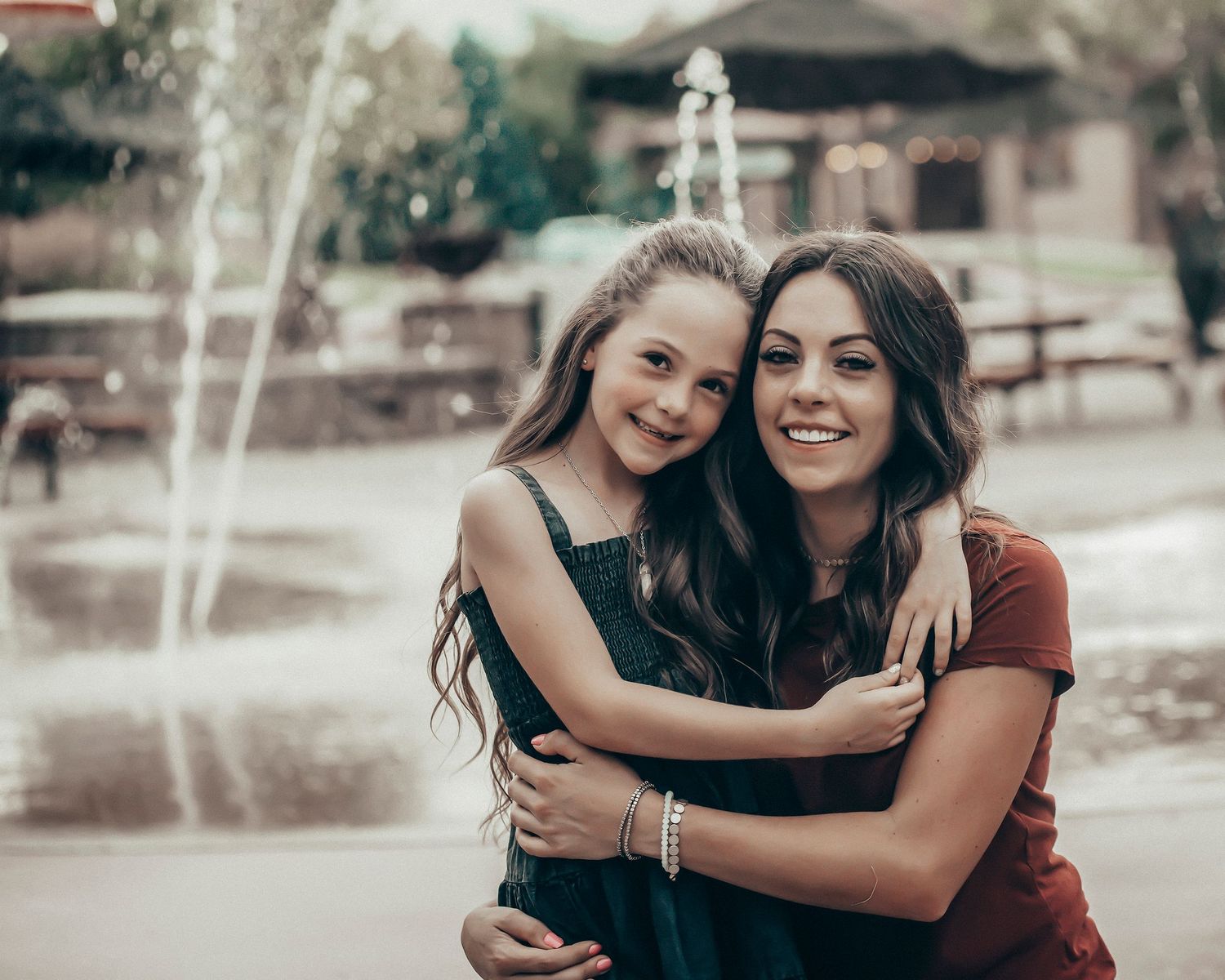 Two people embracing and smiling outdoors near a fountain.