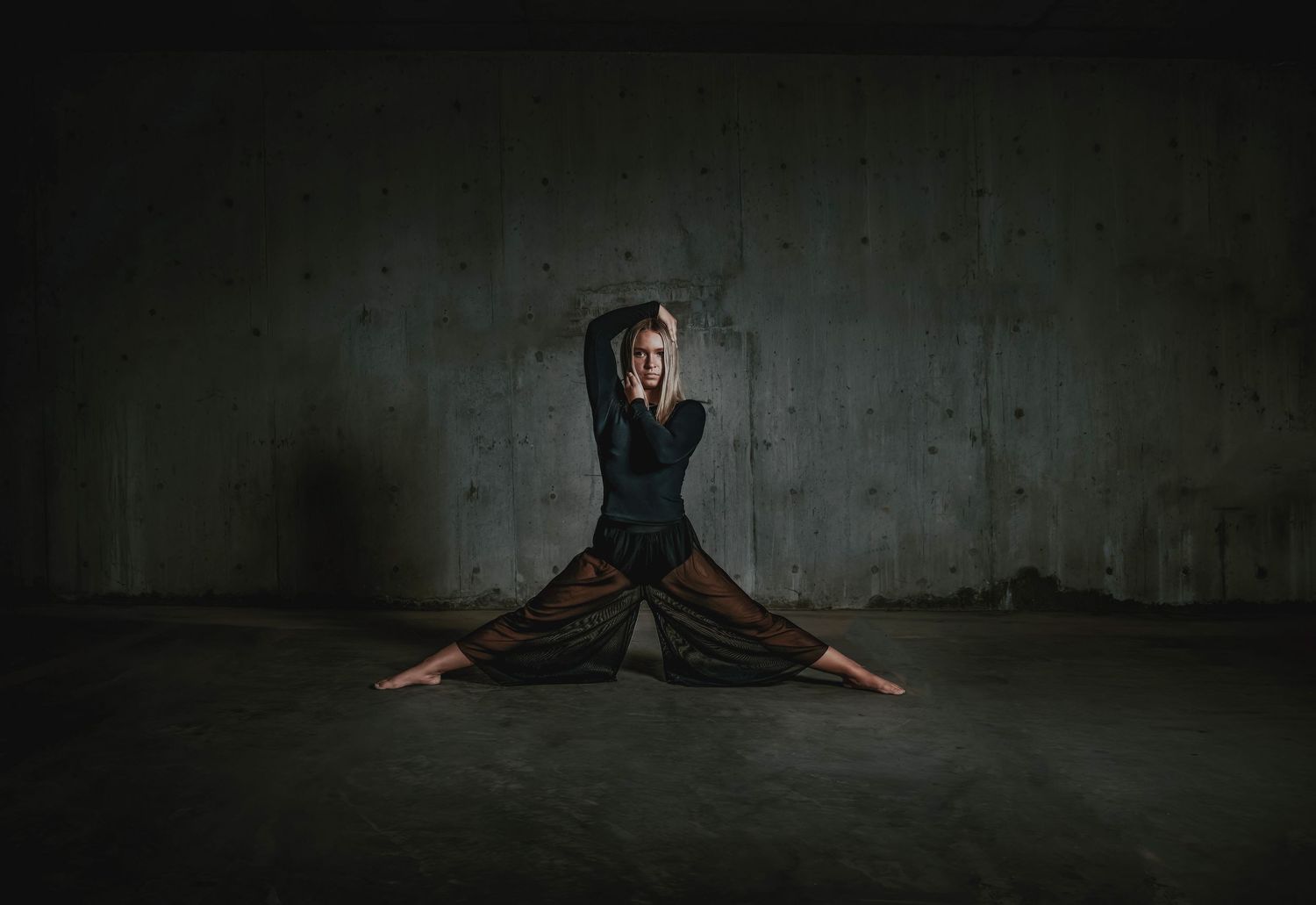 A silhouetted figure performs dynamic dance movements against a dark textured wall in a dramatic artistic series.