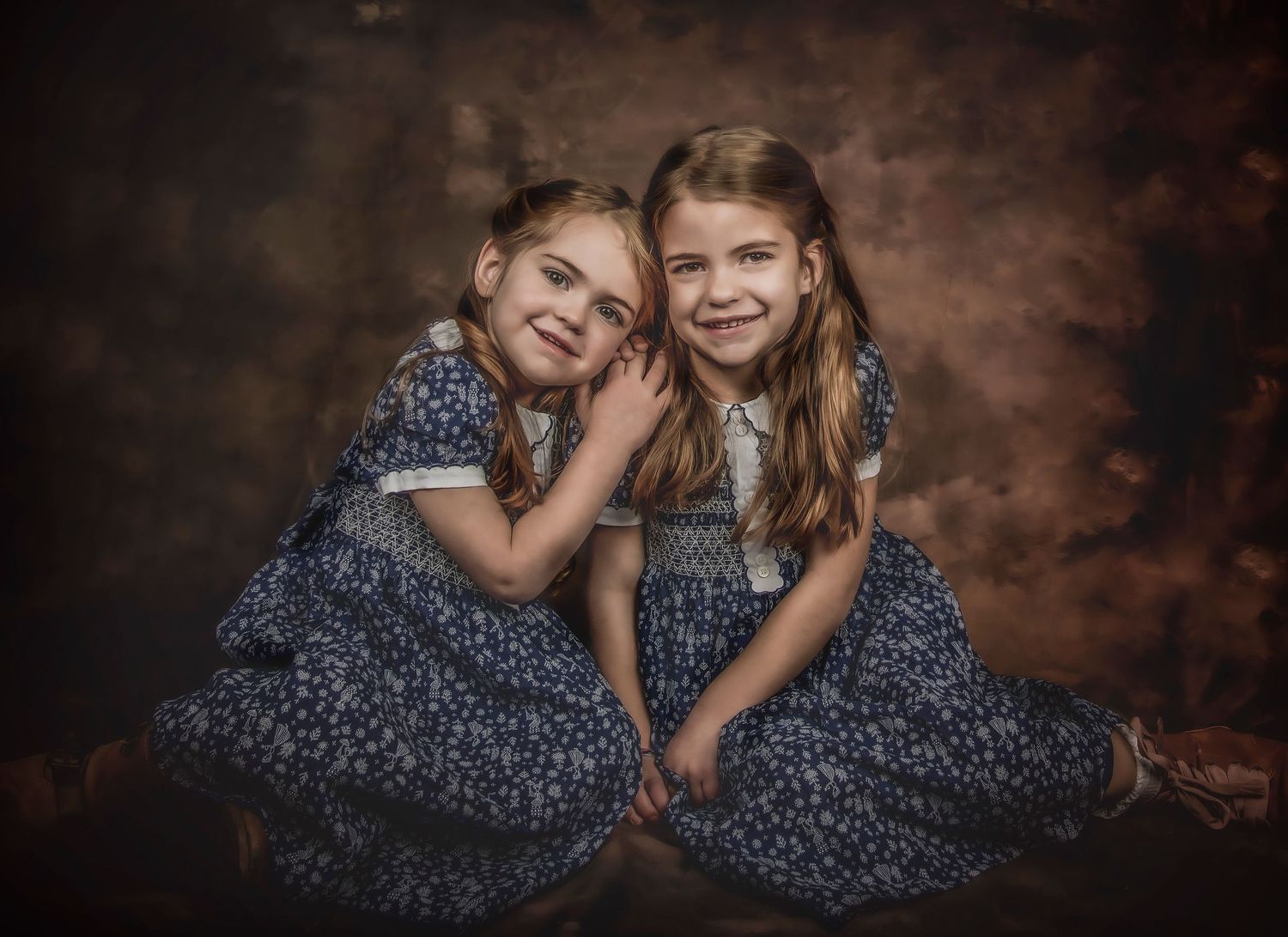 Two children in matching blue floral dresses pose together against a dark studio backdrop.