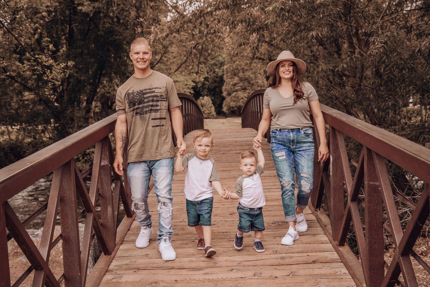 Family walks together holding hands on wooden bridge surrounded by autumn foliage.
